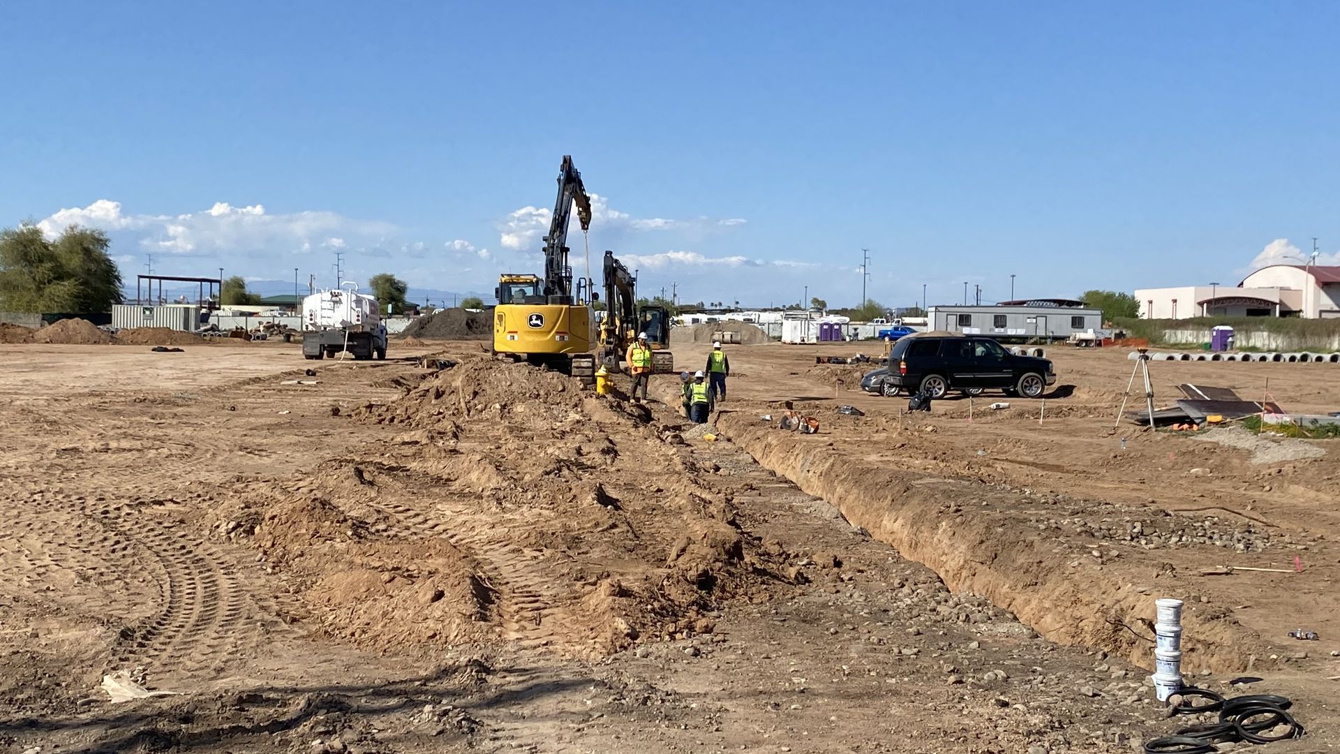 Workers and excavators at a construction site with a trench running through the dirt.