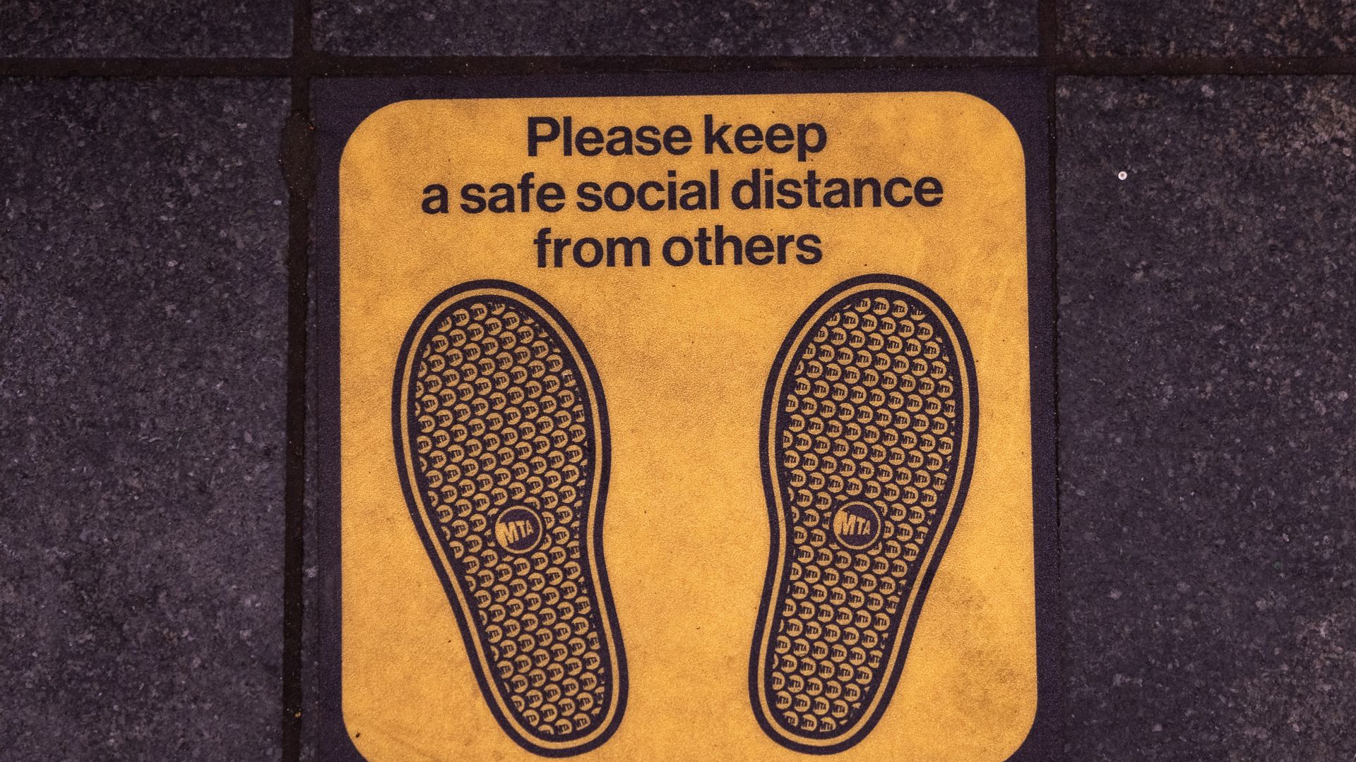 Signage on the floor of the Times Square subway platform asks commuter to maintain a safe social distance