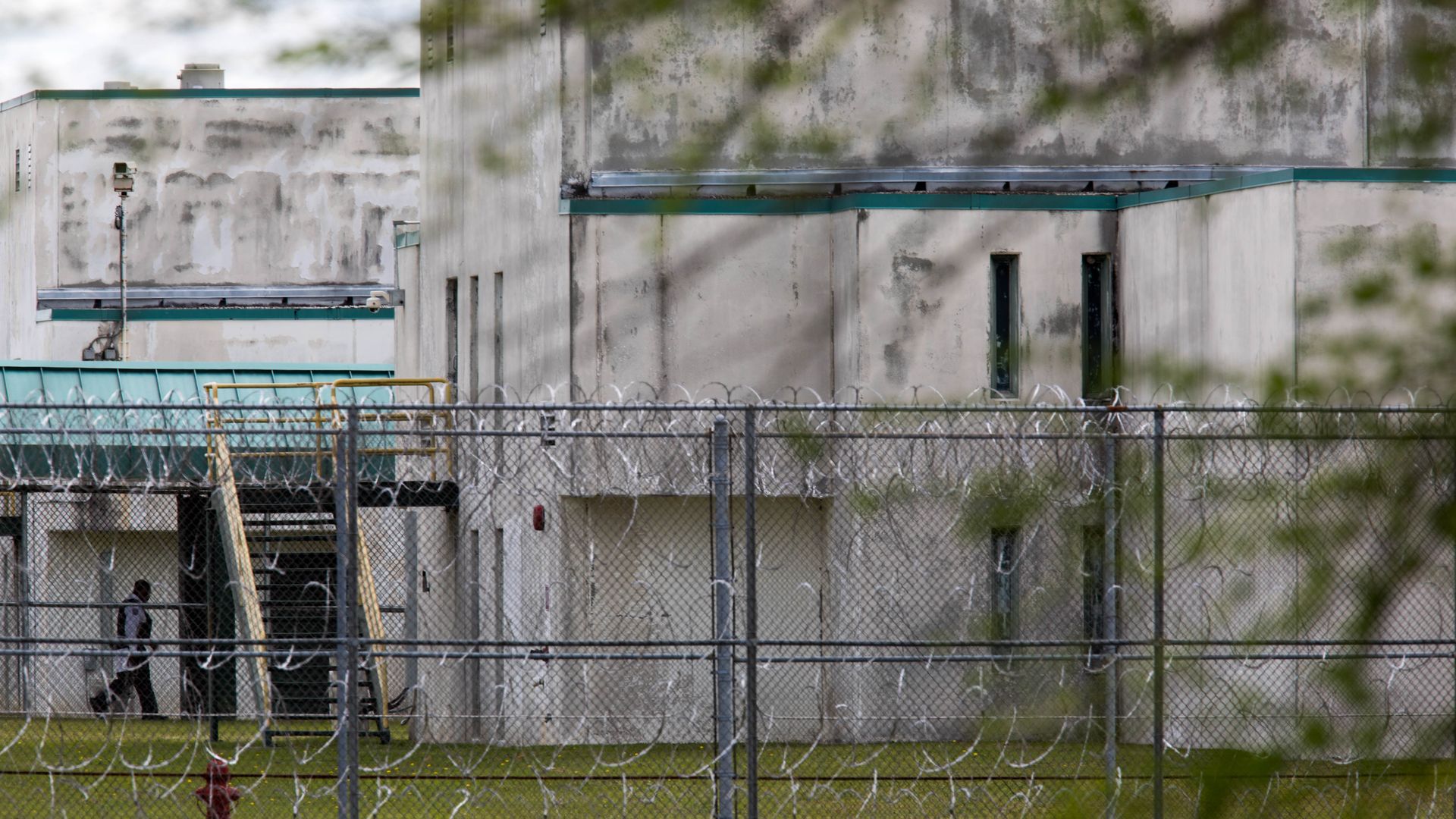 A prison guard runs into a correctional center viewed through a chainlink fence