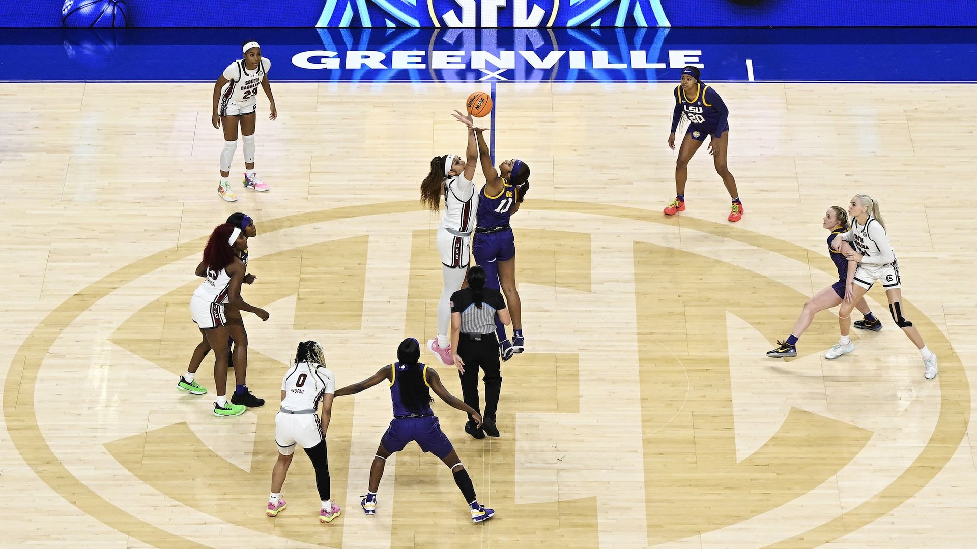 Women's basketball players tip off at SEC game with SEC emblem on the floor.
