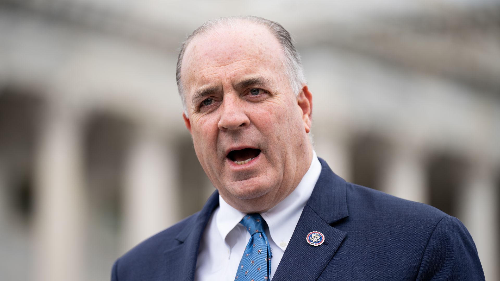 Rep. Dan Kildee, wearing a blue suit, white shirt and light blue tie, standing in front of the U.S. Capitol.