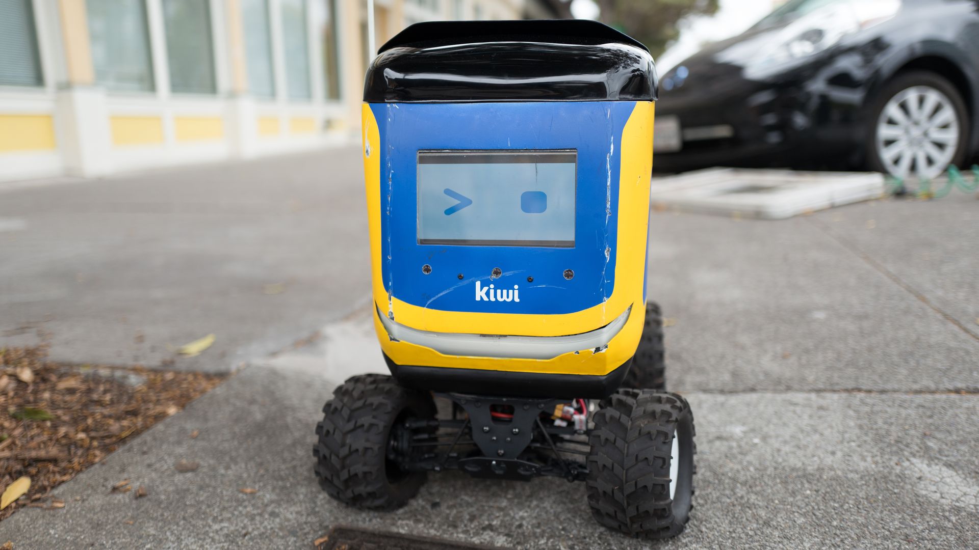 Front view with digital face of Kiwi self driving autonomous package delivery robot parked on a street corner in Berkeley, California