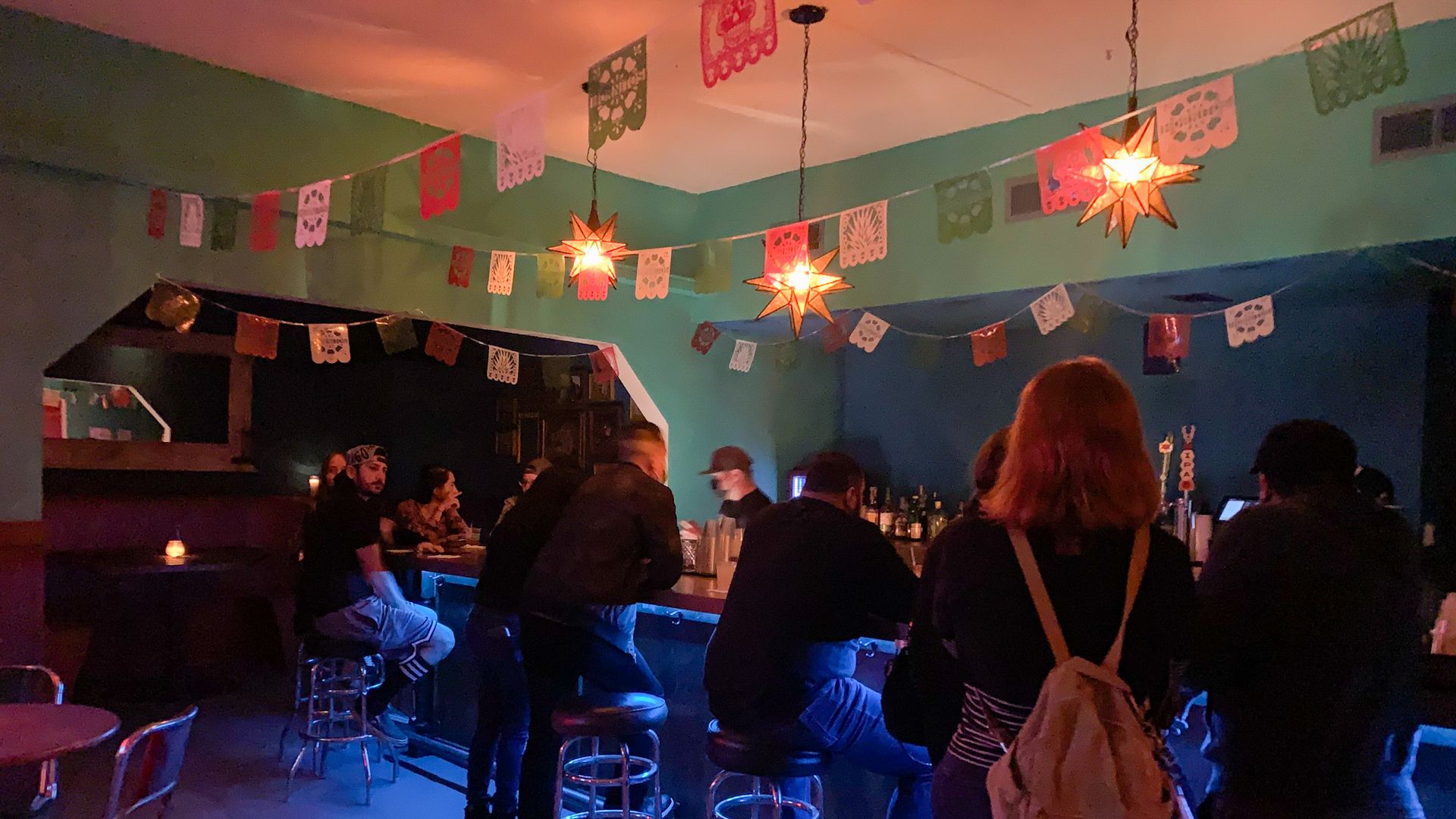 A bar with teal walls and papel picado hanging from the ceiling.