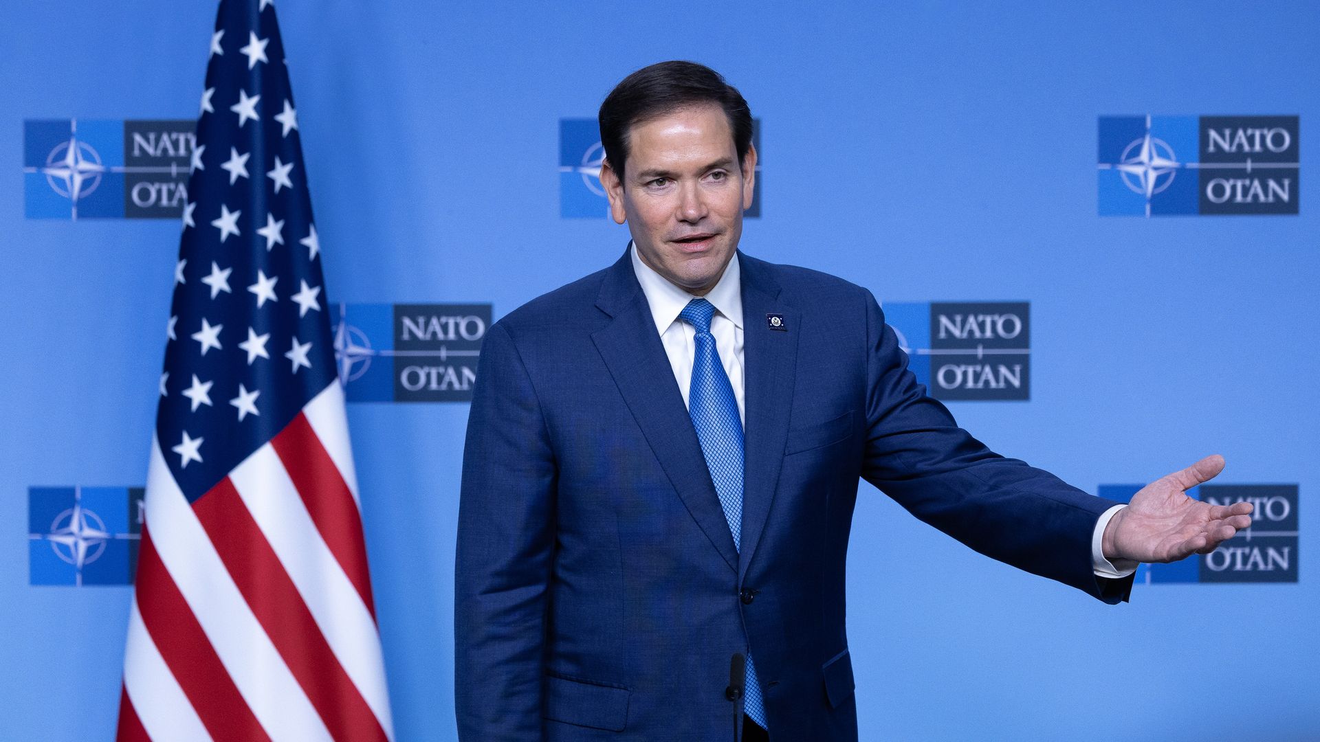 Marco Rubio gestures as he speaks in front of an American flag.