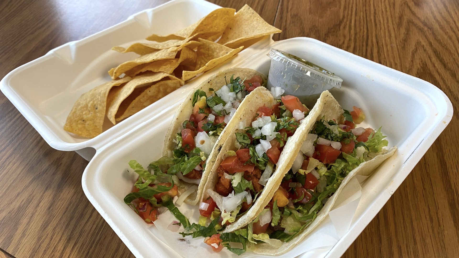 Three tacos in a foam container with chips