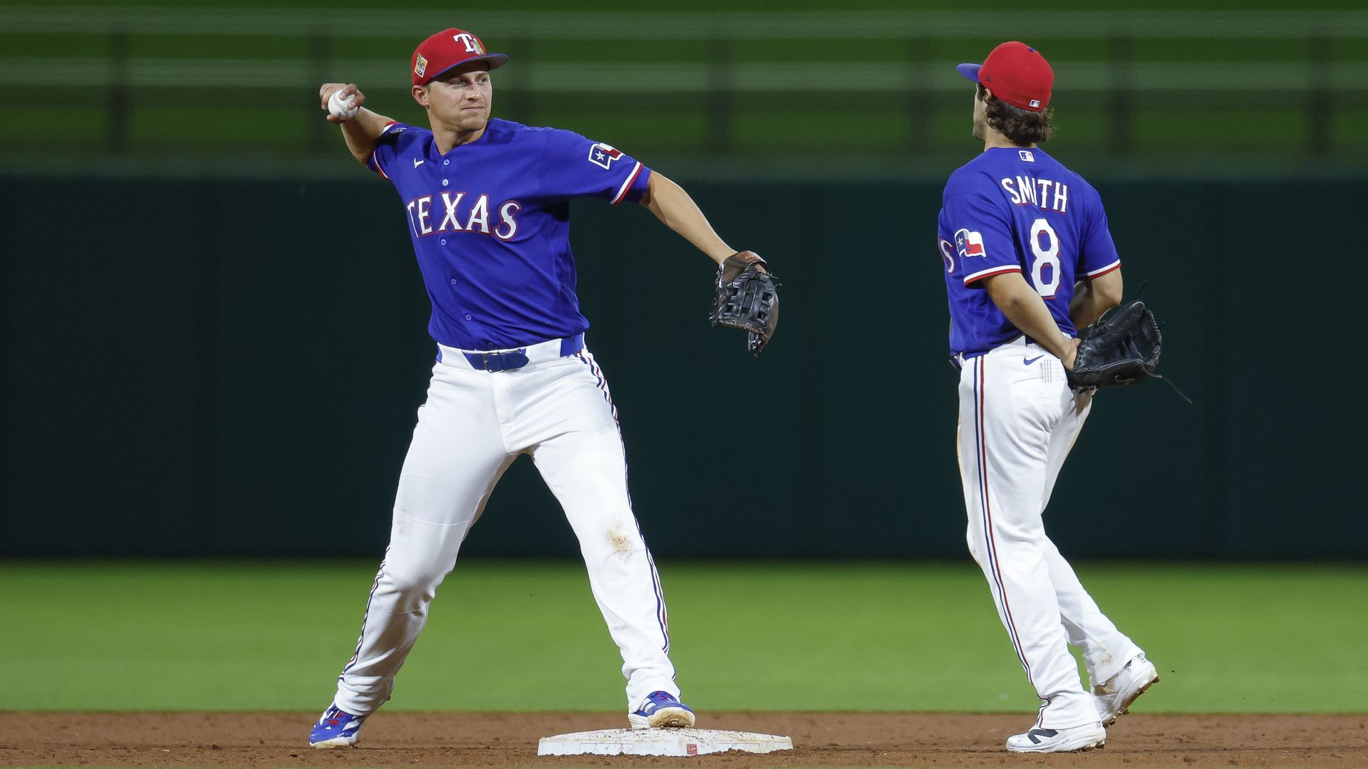 Corey Seager #5 of the Texas Rangers throws to first base during a Spring Training game against the Kansas City Royals while Josh Smith has his back to the camera. 