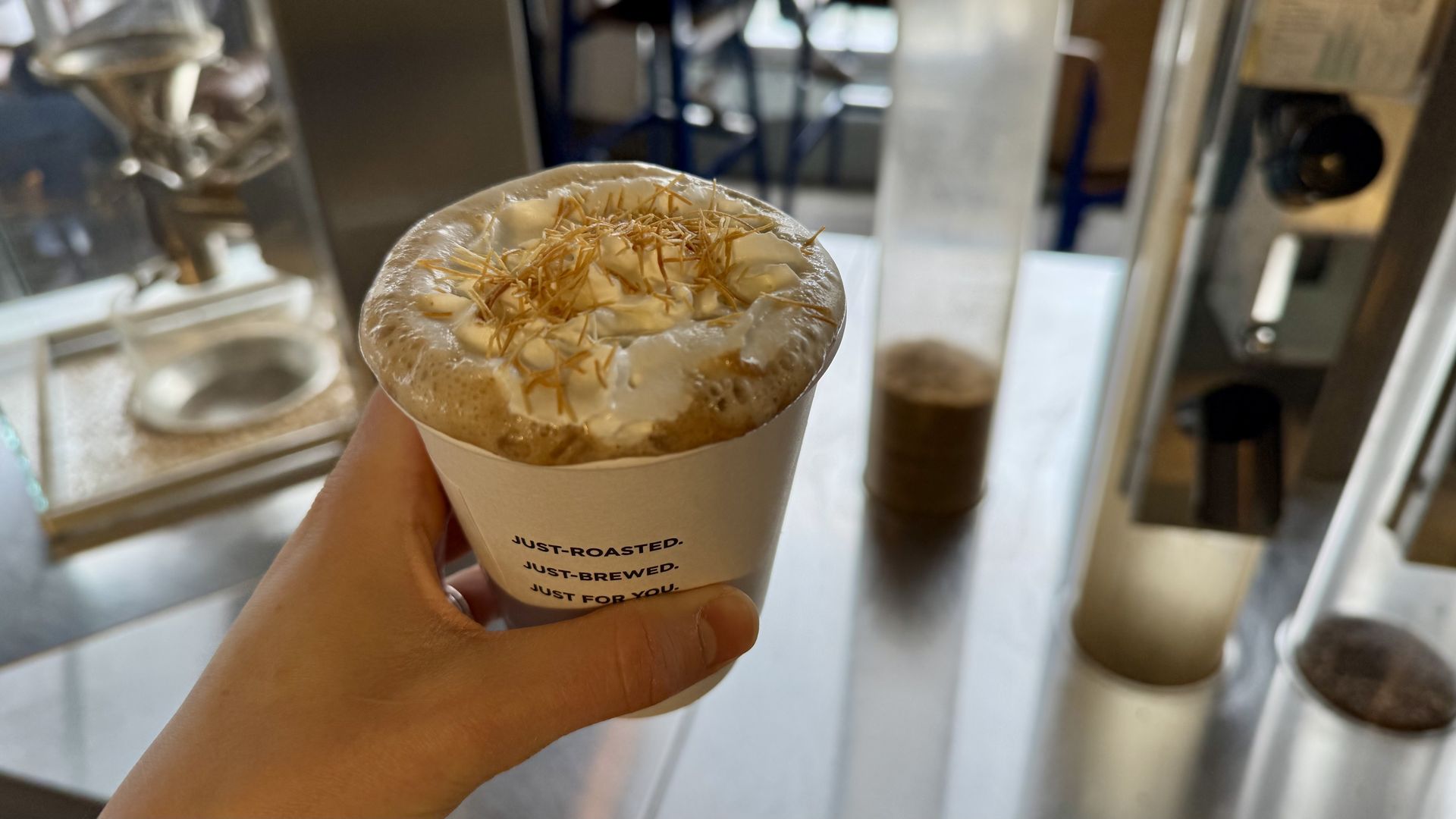 A mocha in a to go cup with a crunchy sprinkling on top of whipped cream