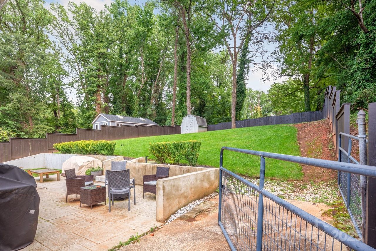 Bright kitchen with white cabinets, stainless steel appliances, and wood flooring. Potted plants by fridge and window, white island with two stools, and a beige rug on the floor.
