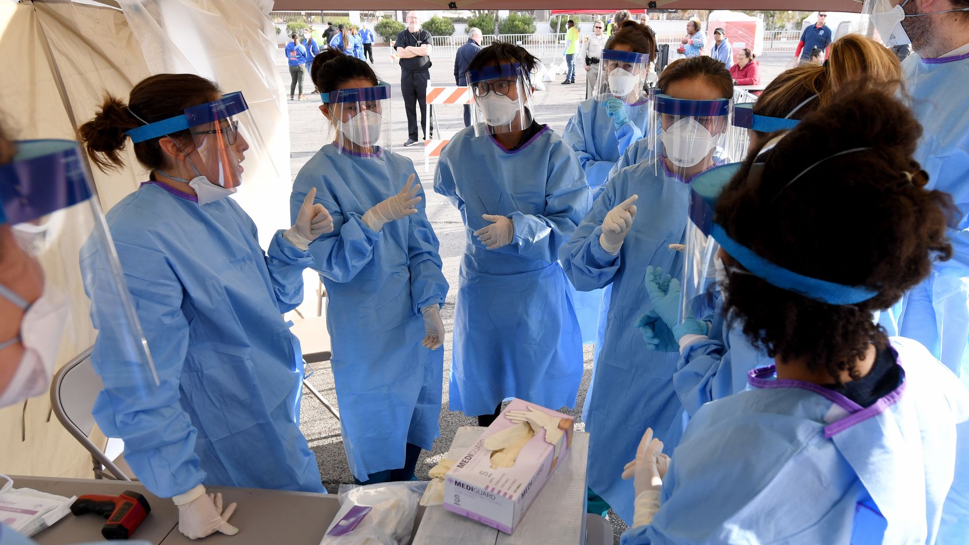 Medical workers dressed in blue gowns and face masks stand in a tent, ready to test people for coronavirus.