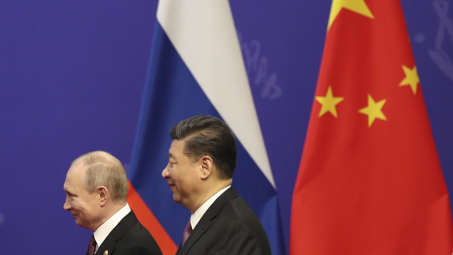 Vladimir Putin and Xi Jinping in front of two flags.