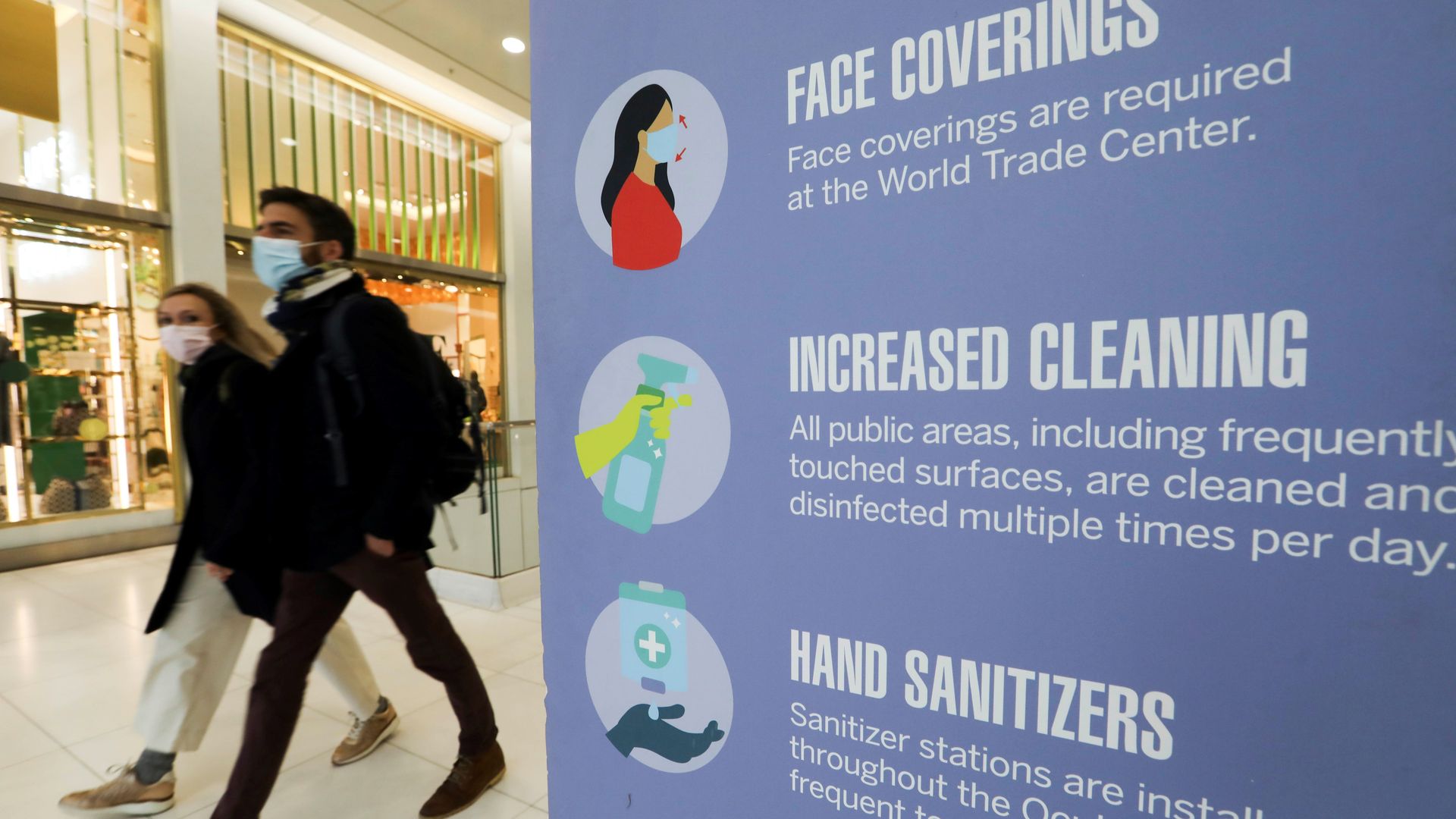 People walk past a signboard with COVID-19 control measures at the World Trade Center in New York.