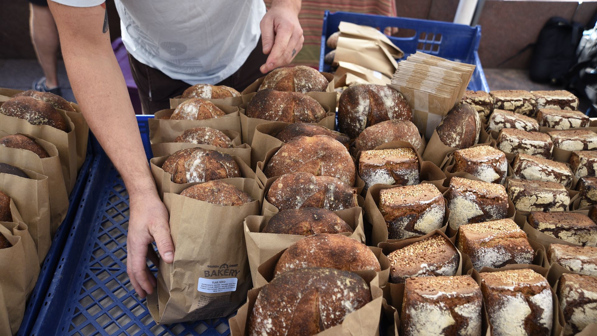 Several bread loafs in small packaging close to one another while a hand reaches down to grab one. 
