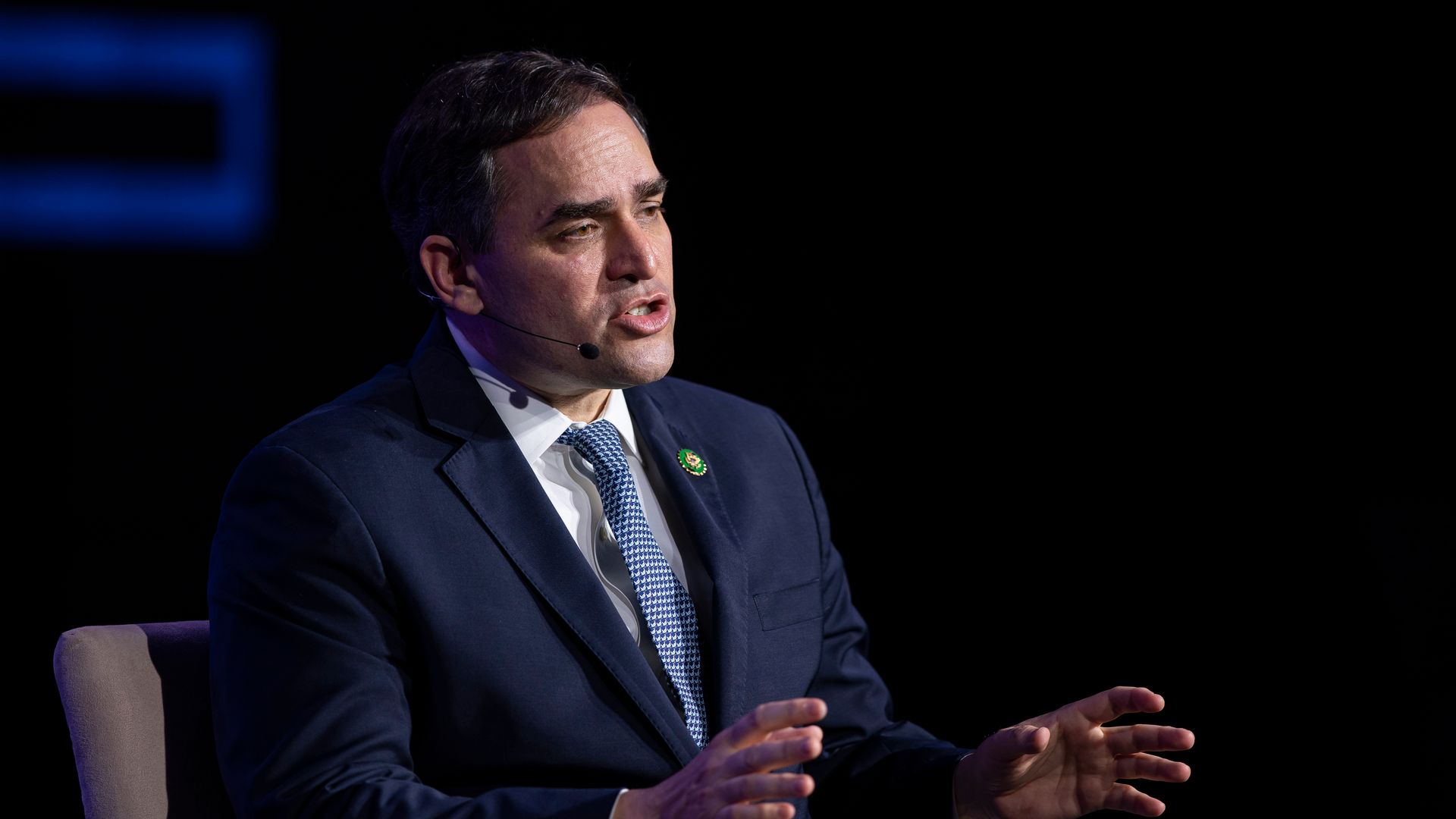 Rep. Wiley Nickel wearing a blue suit and sitting on a chair in front of a black backdrop.