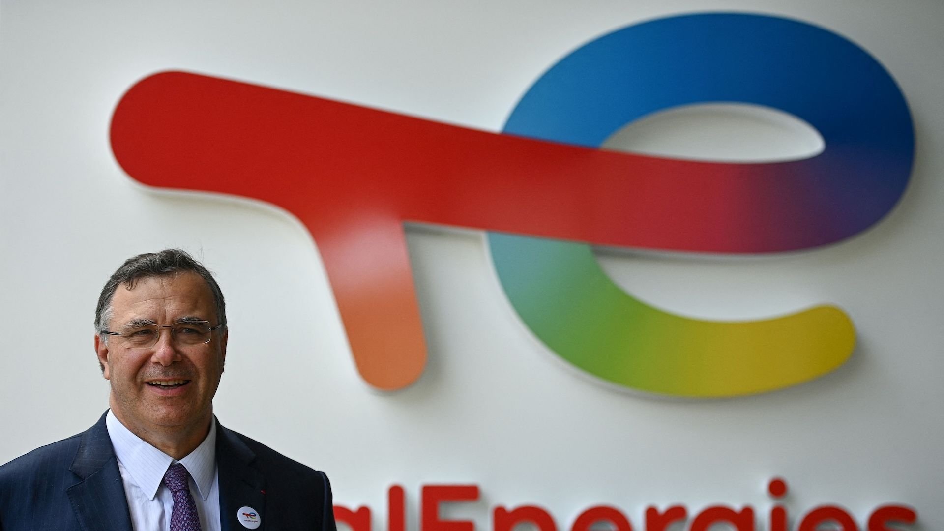 Photo of TotalEnergies CEO Patrick Pouyanné standing in front of the company's logo