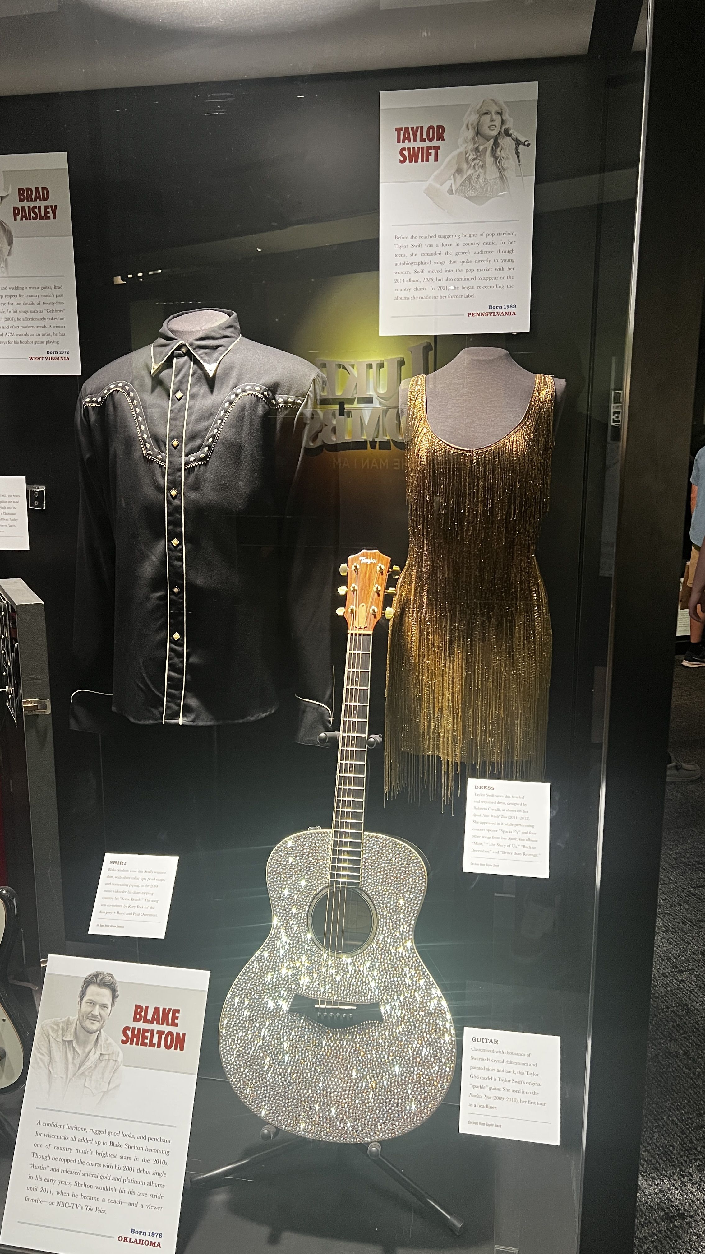 A shirt, dress and guitar behind a glass case. 