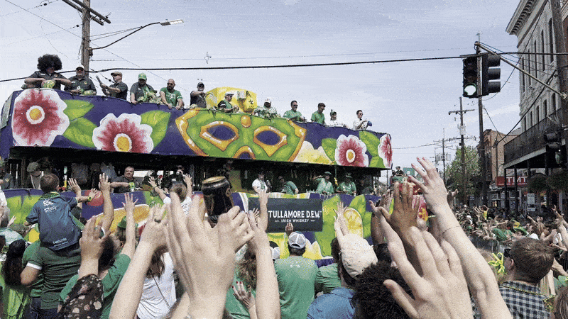 A gif of a St. Patrick's Day float crossing Magazine Street. People wave their hands to try to catch throws, and float riders toss beads.