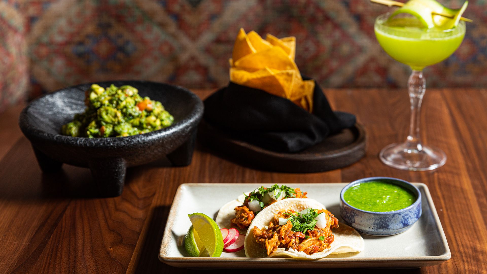 A table with plates of tacos, chips and guacamole on it.