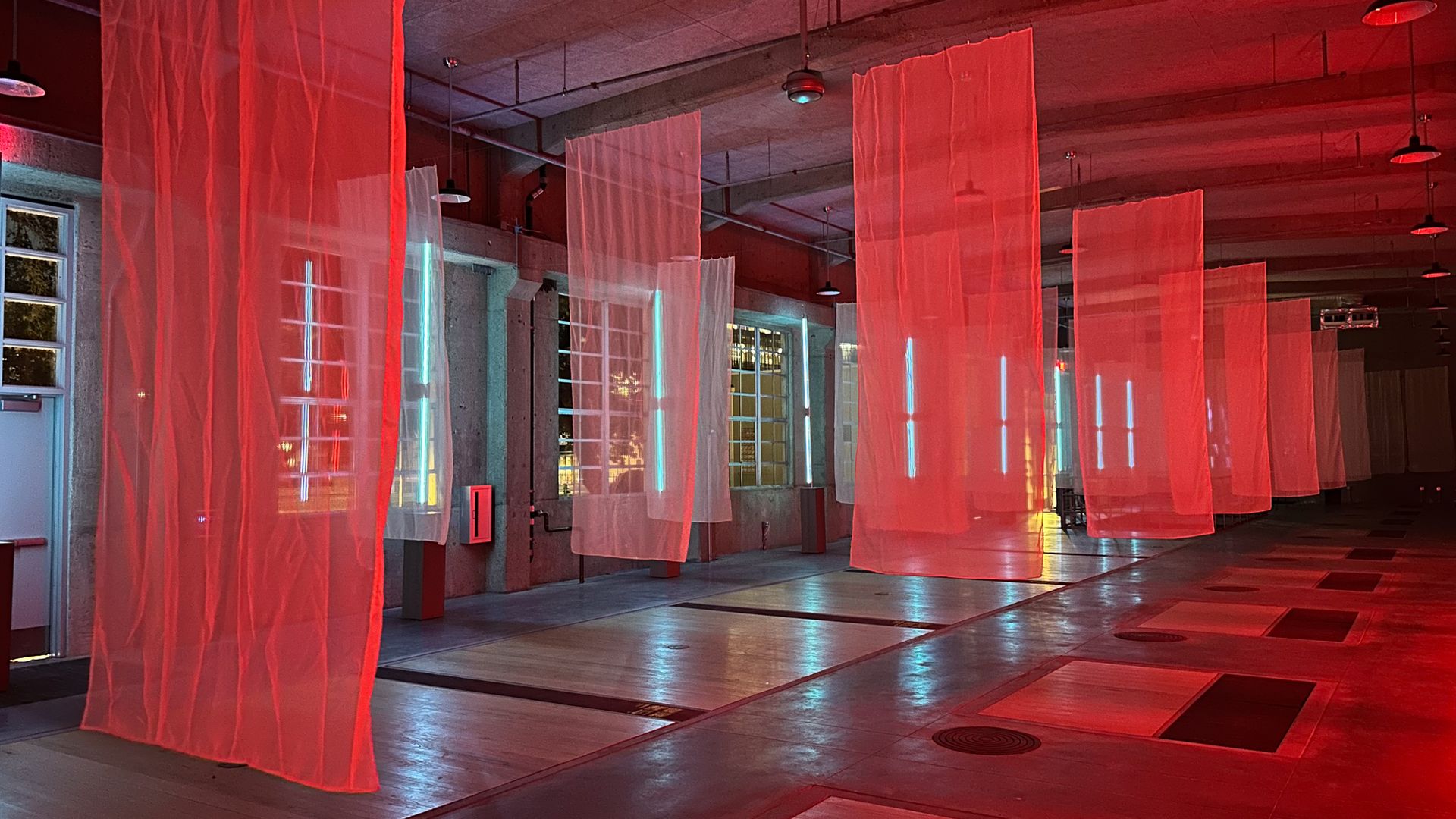 A photo of fabric hanging from the ceiling, with red light illuminating them.