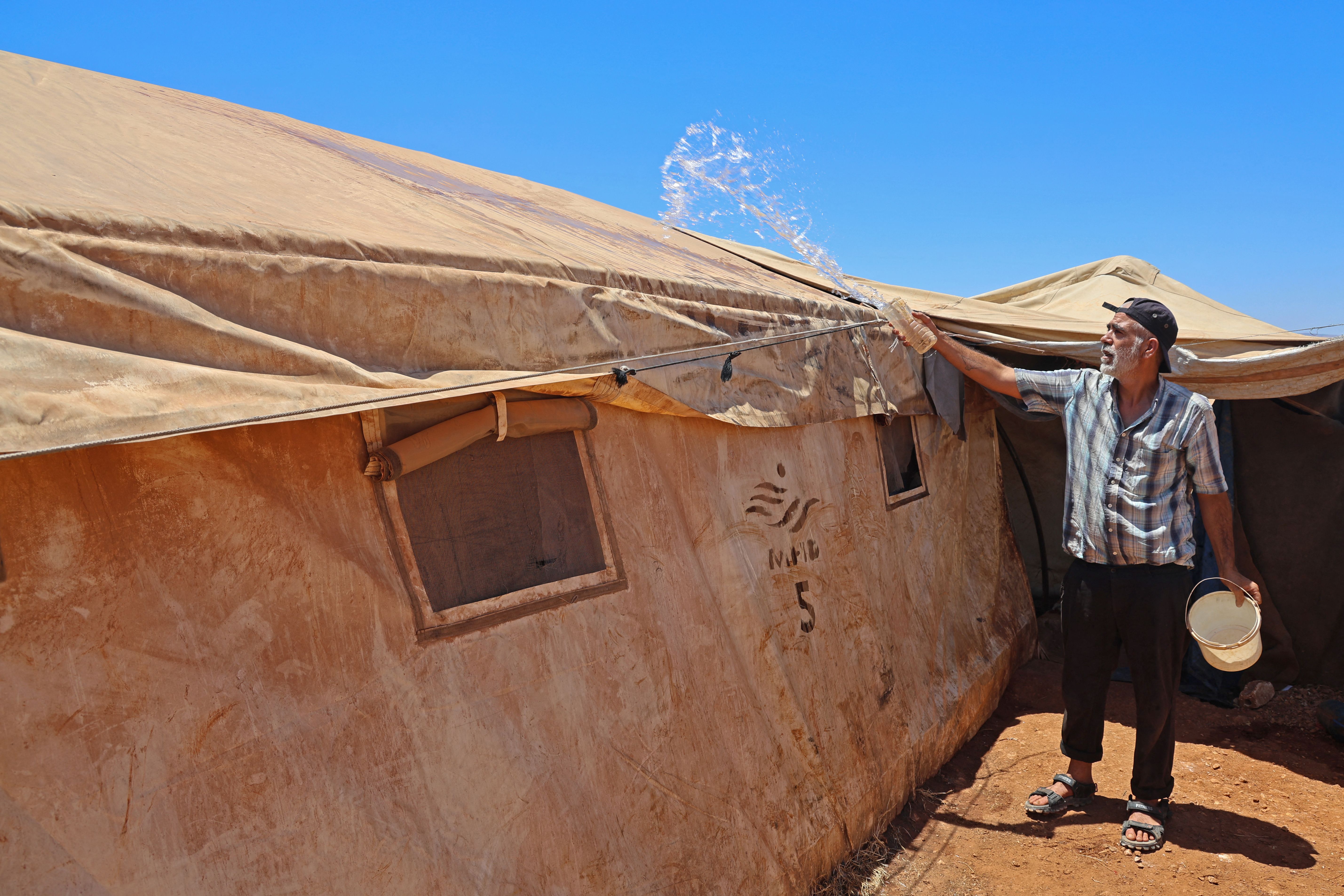 A man pours water on his tent to provide relief from the extreme heat at the Haranbush camp for displaced people in Syria's northwestern rebel-held Idlib province on July 19, 2023. 