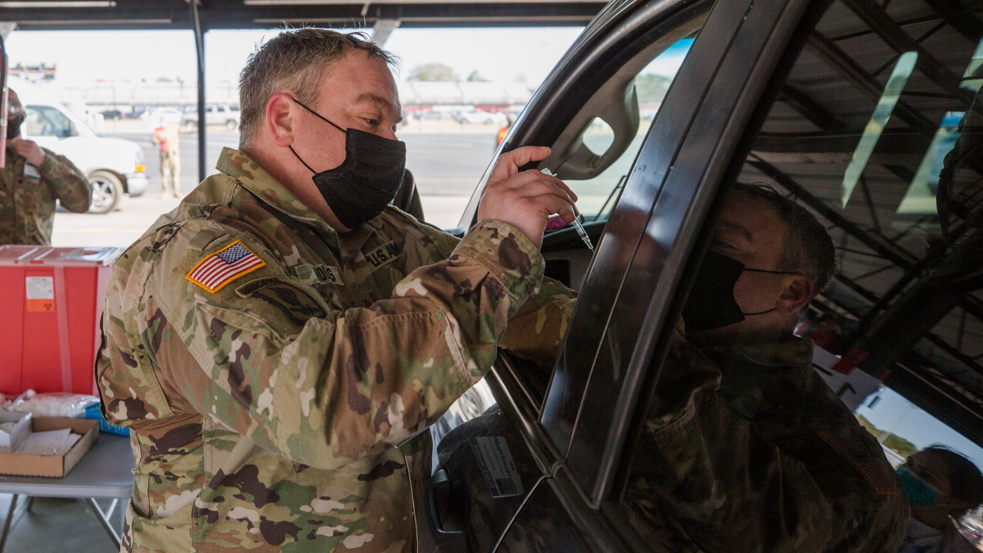 A man in an Army uniform stands outside a car