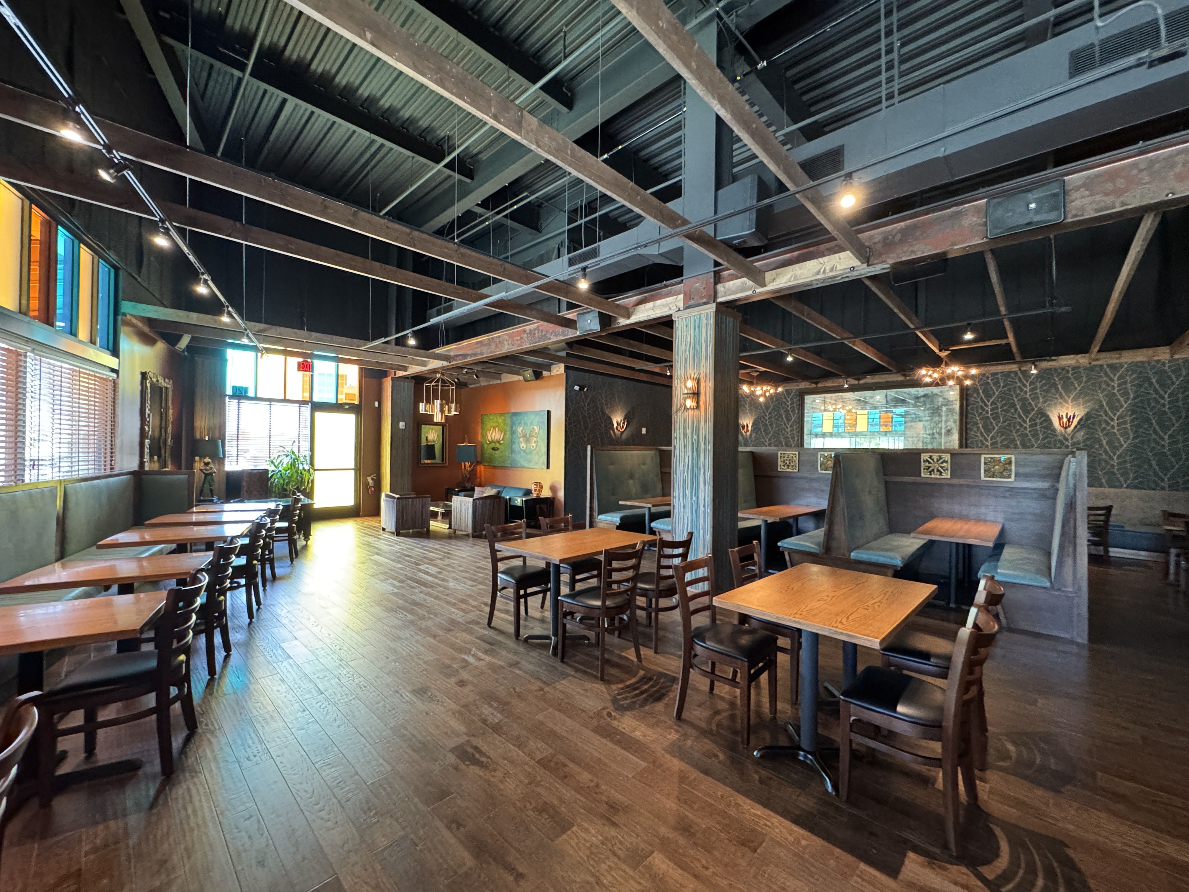 Empty restaurant with wooden tables, chairs, and booths, decorated with stained glass windows, exposed ceiling beams, and warm lighting.