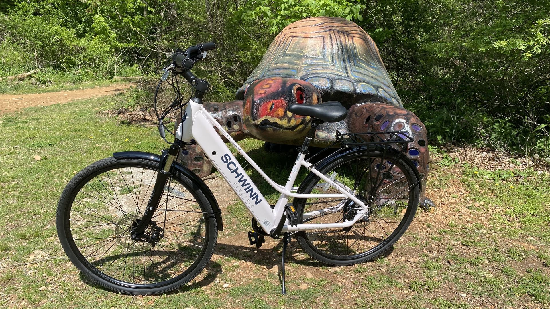 A white bicycle stands in front of a giant statue of a turtle. 