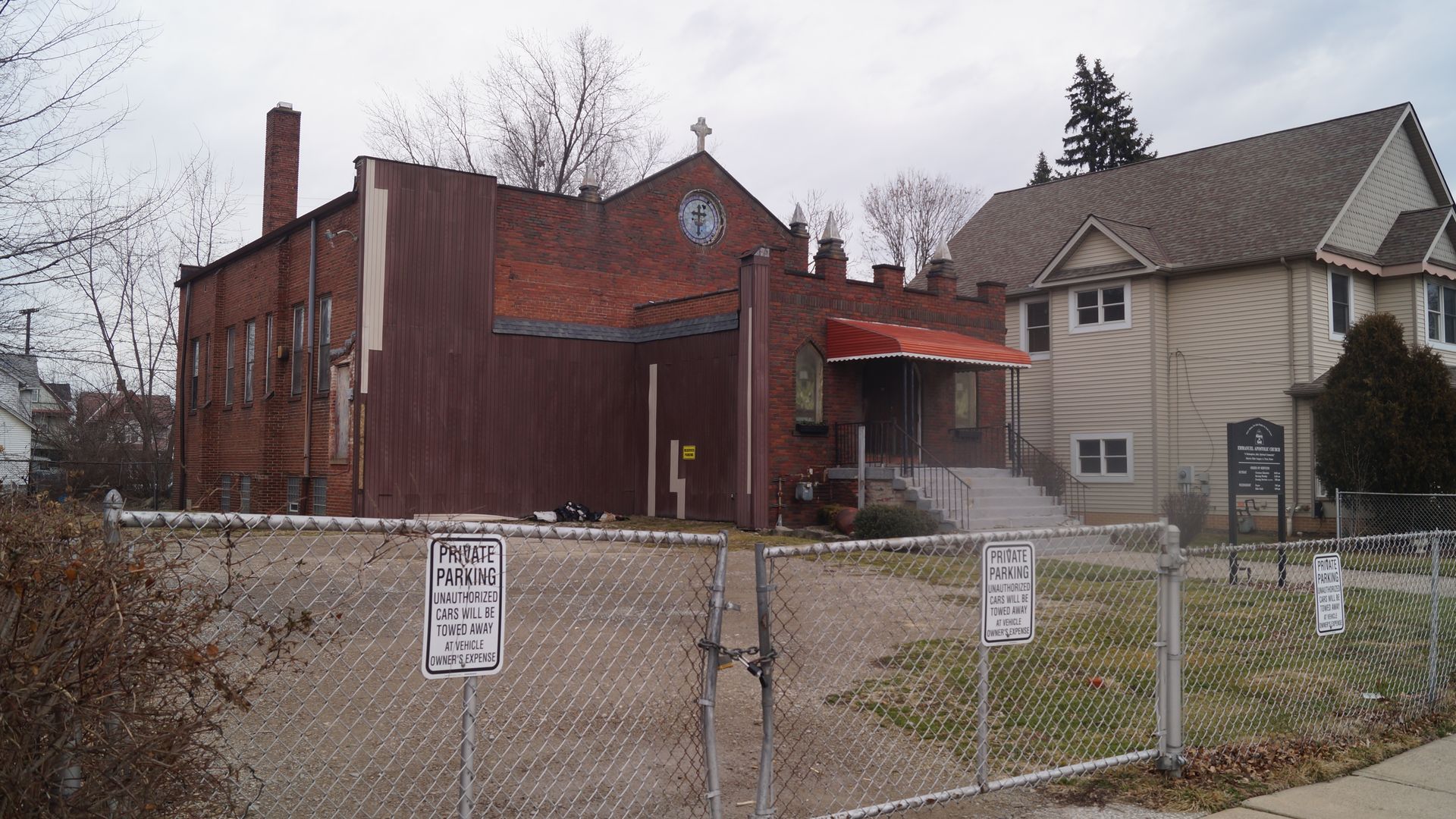 An abandoned red brick church next to an empty lot.