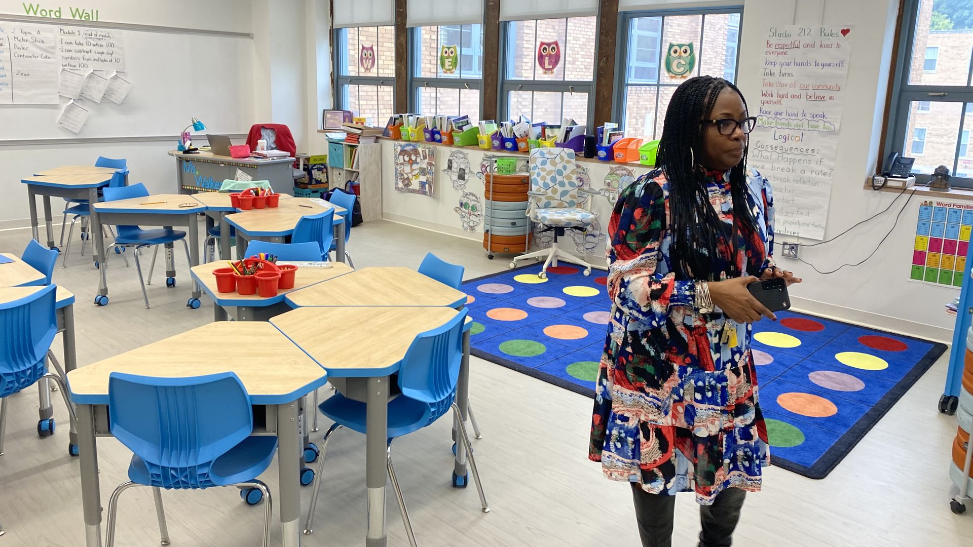 The Marygrove principal stands in a classroom with chairs, tables, a big mat, windows and bright colors. 