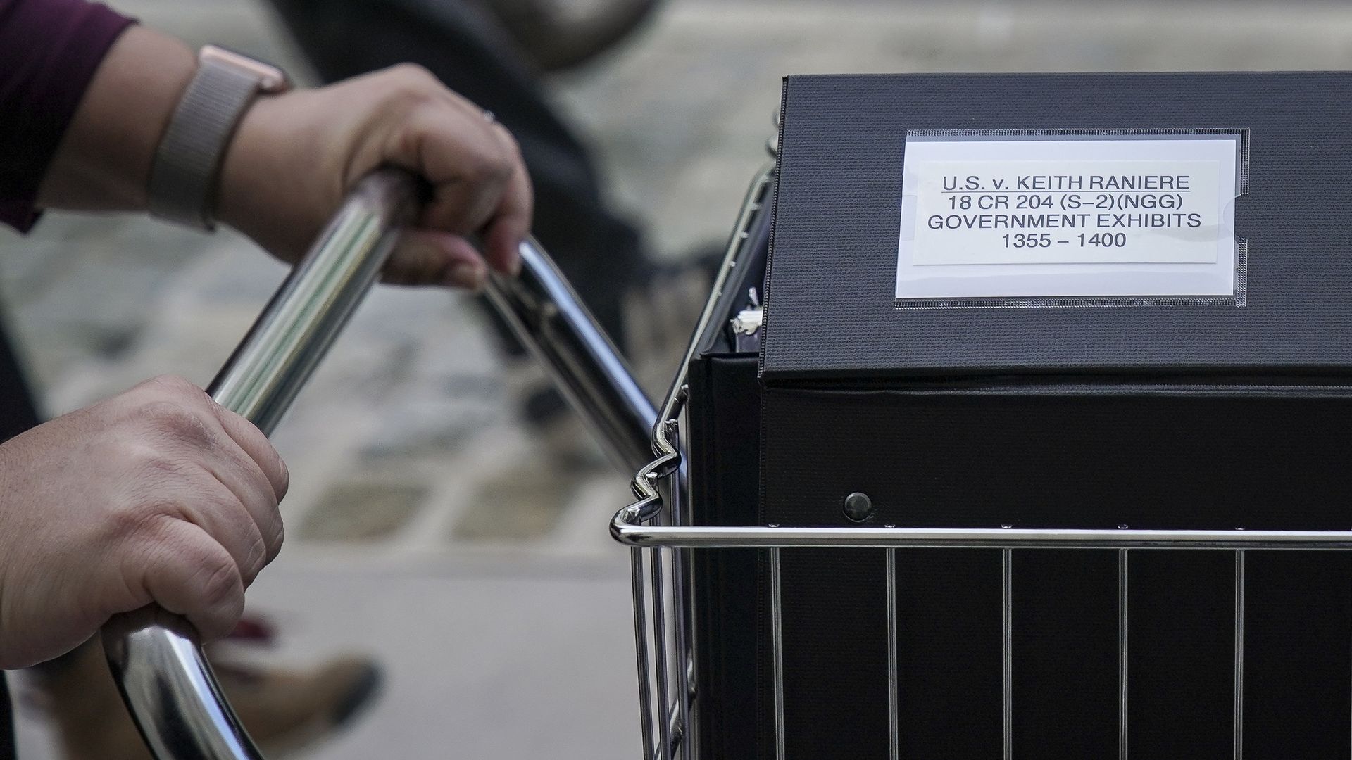 Photo of a person pushing a cart with a black box containing court documents related to Keith Raniere
