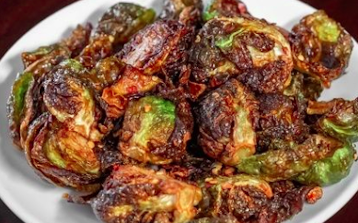 A white plate piled with charred, crispy roasted Brussels sprouts, their green centers peeking through the browned exterior.