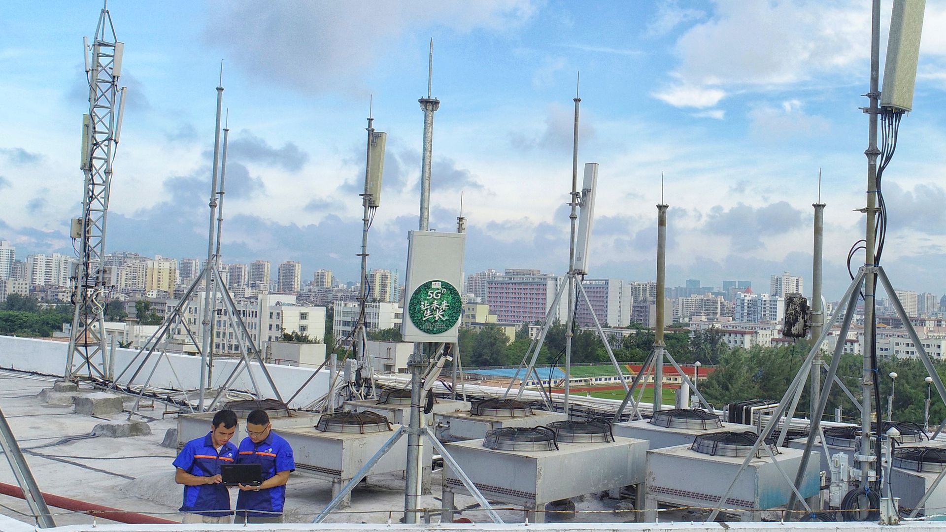 Two men consult equipment on a rooftop surrounded by 5G antennas
