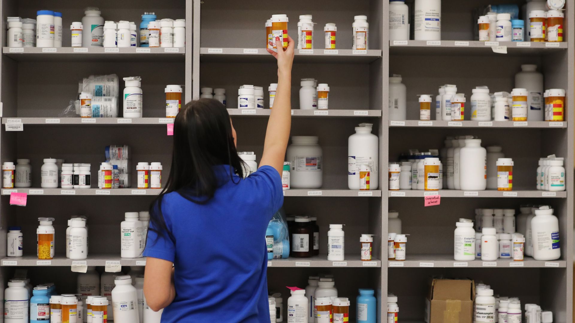 A pharmacy technician grabs a bottle of drugs off a shelve