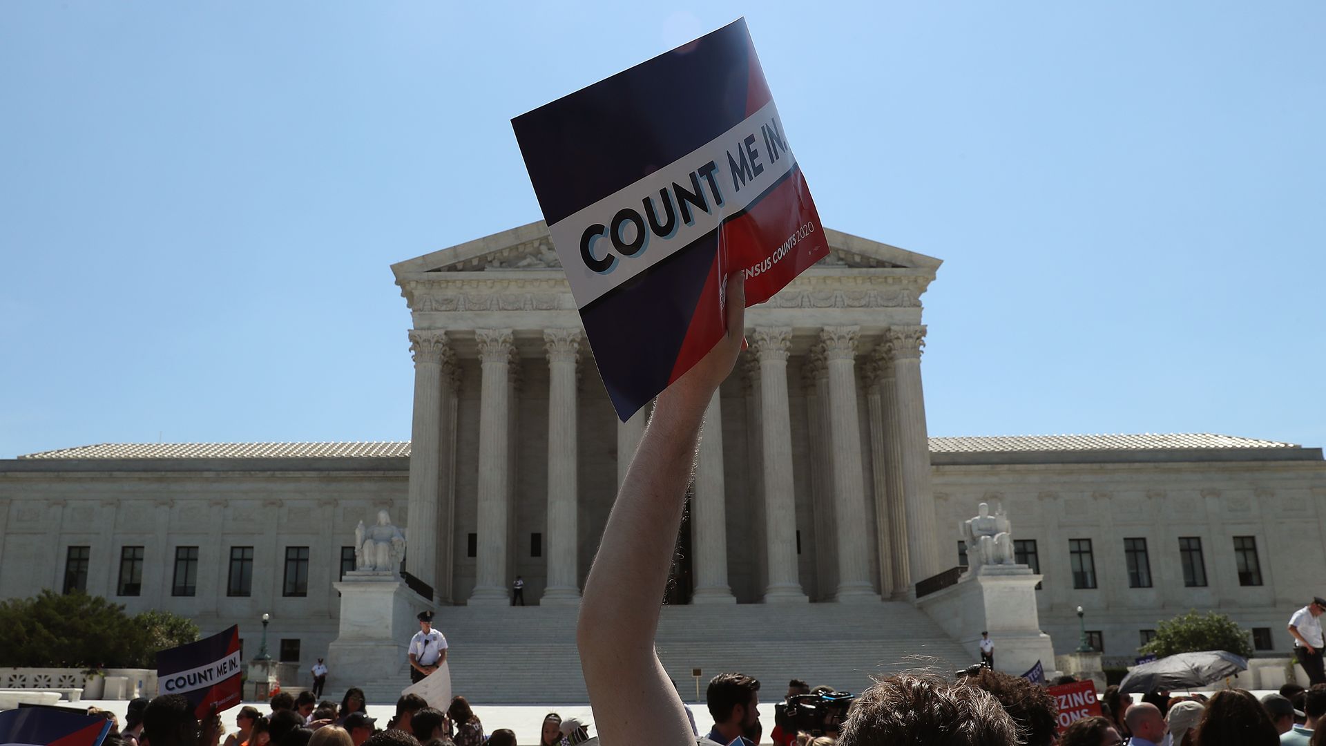 This image shows a man holding a "Count Me in" sign in front of the Supreme Court at a protest.