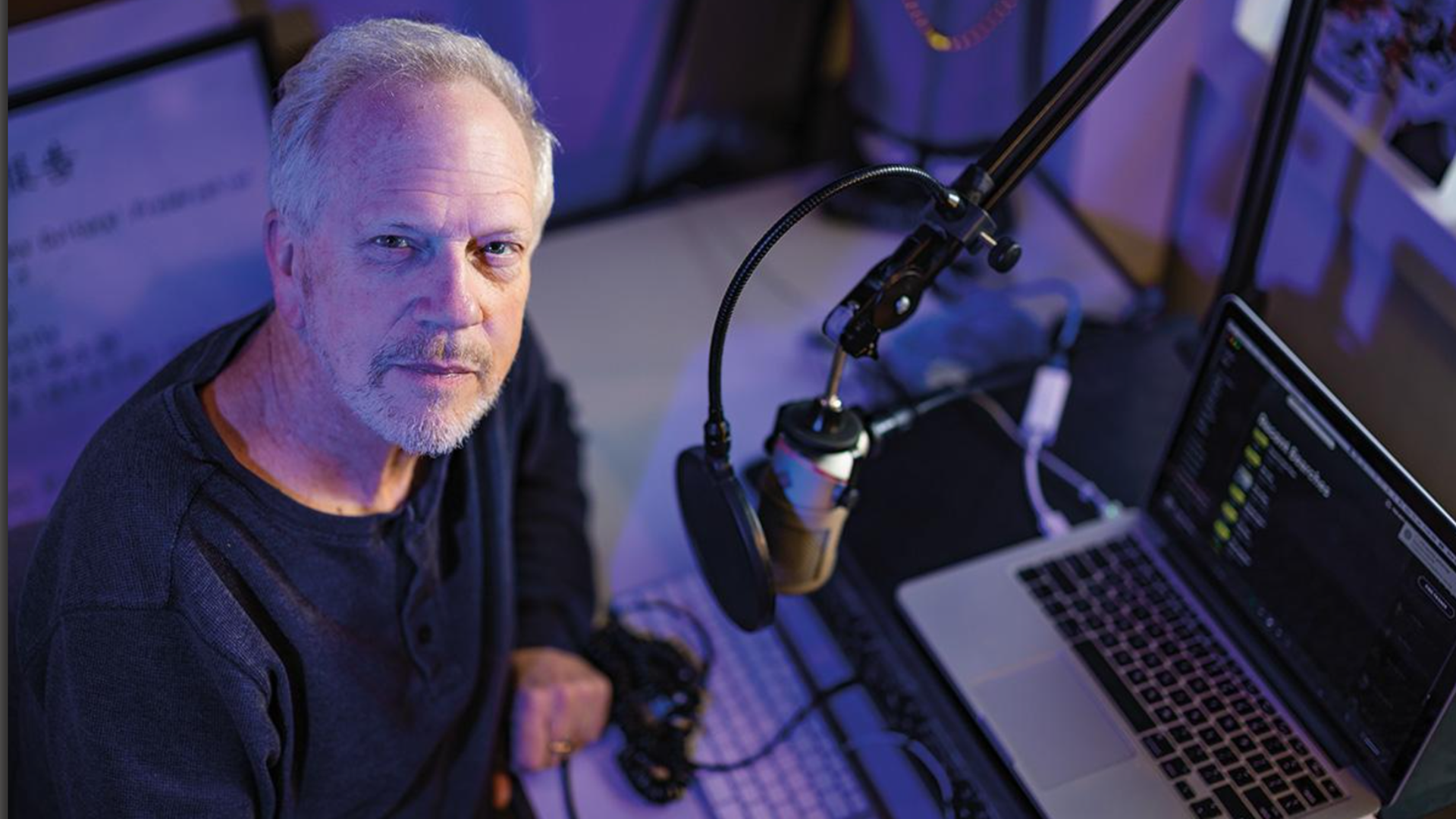 Nick Spitzer poses for a photo in front of a microphone in a recording studio.