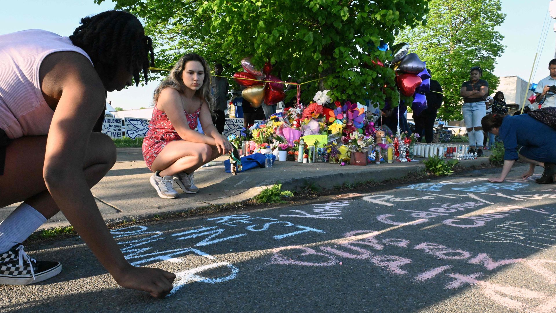 Photo of people leaving messages in chalk on sidewalk and street as a memorial to Buffalo shooting victims