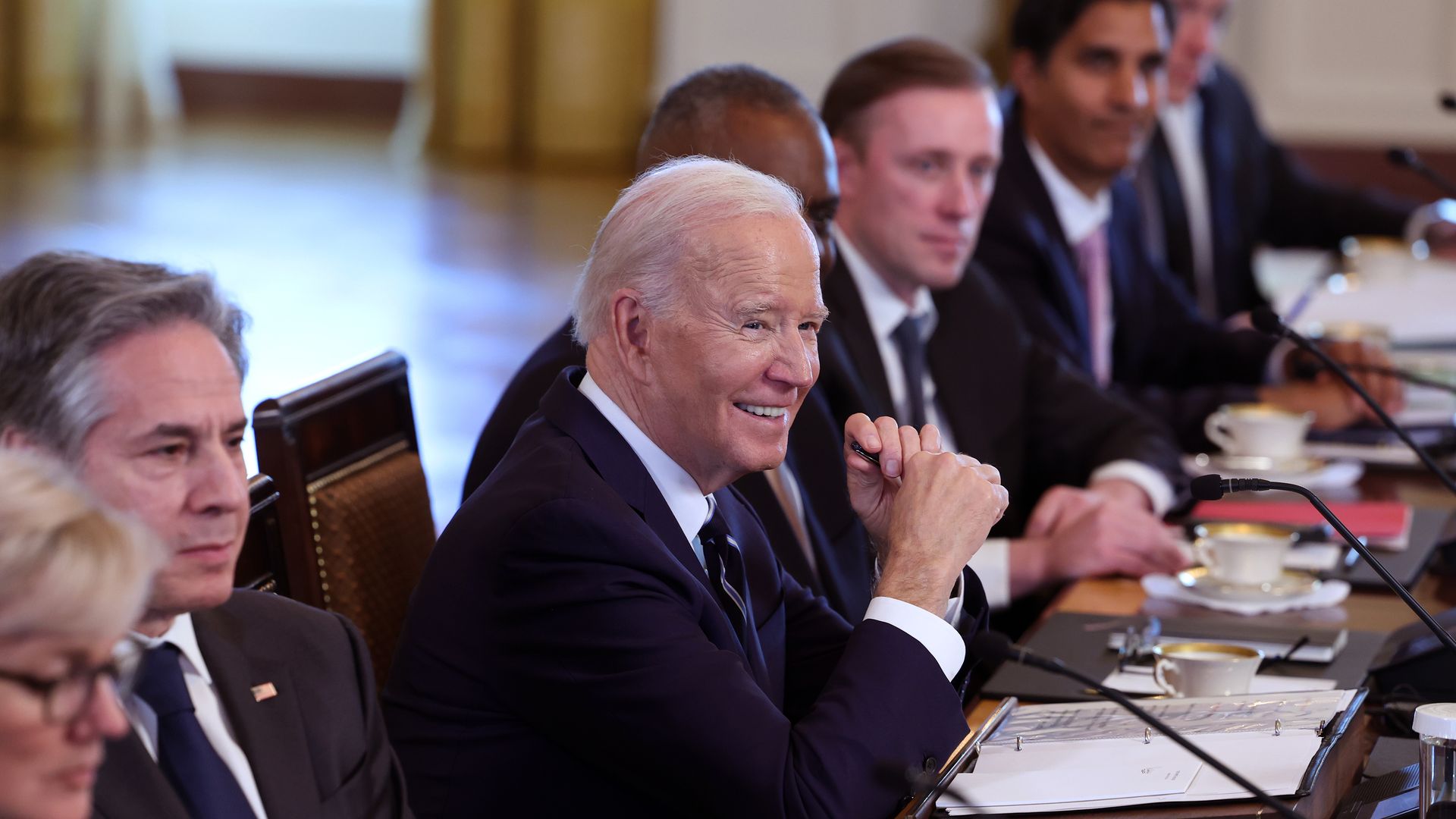 President Biden is shown sitting at a long table at a meeting with others.