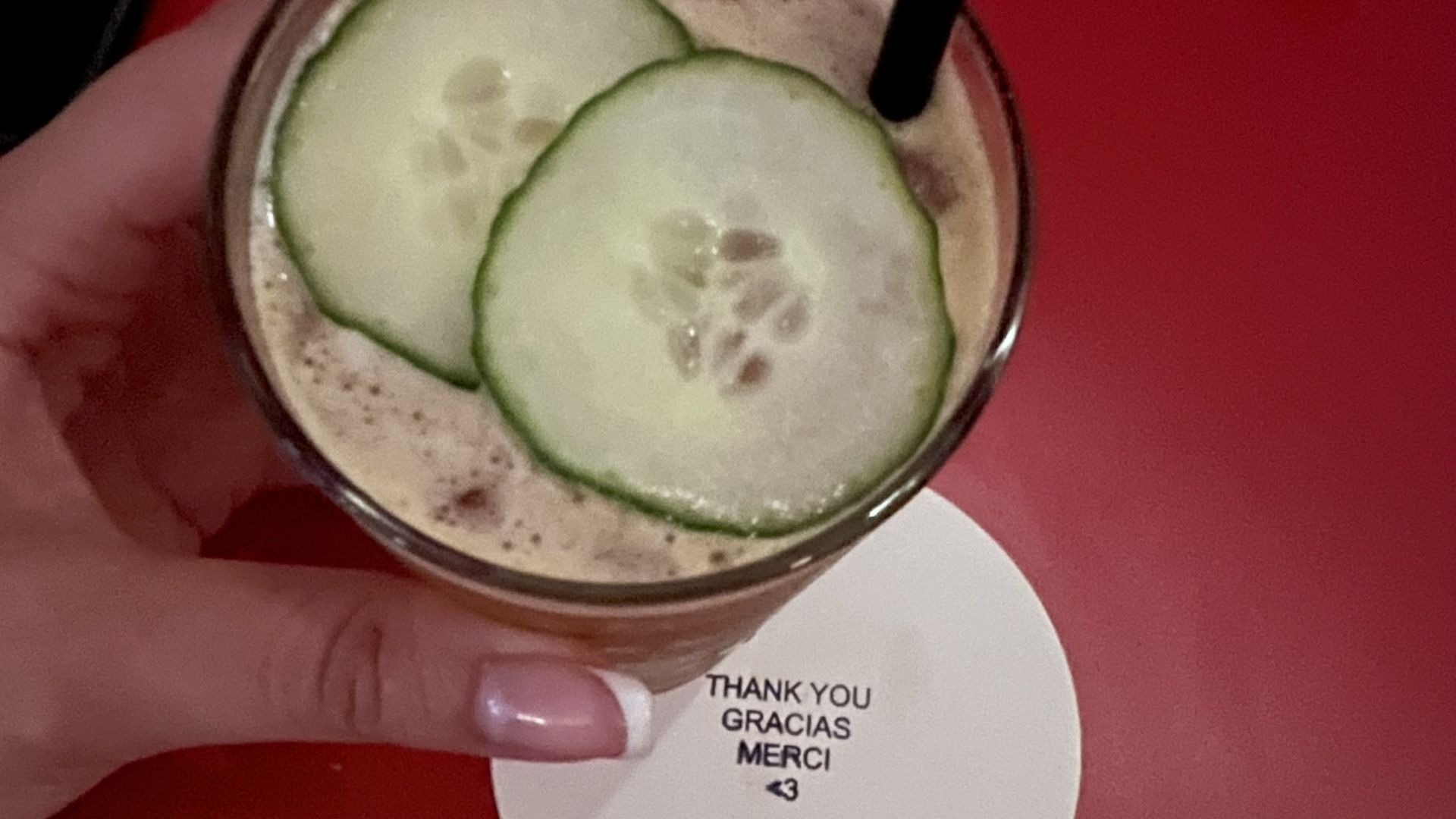 A hand holding a cocktail garnished with two sliced cucumbers. 