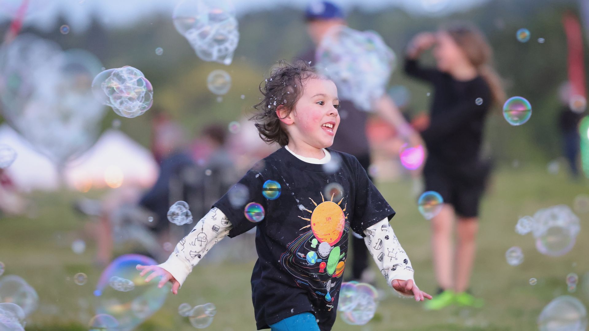 A young boy chases bubbles in a field surrounded by other kids.