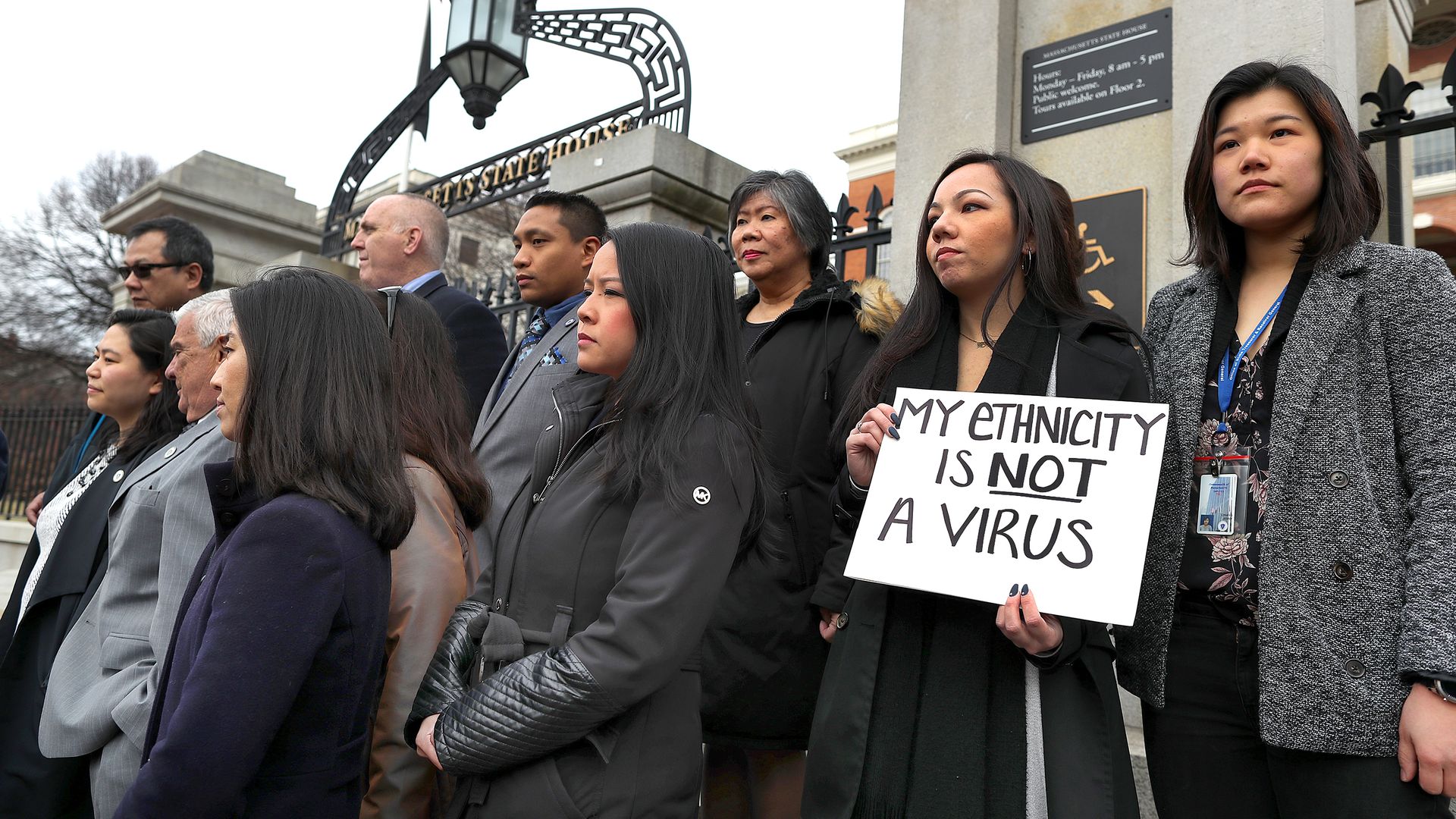 Members of the Asian American Commission hold a press conference in Boston as one woman holds a sign that says "My ethnicity is not a virus."