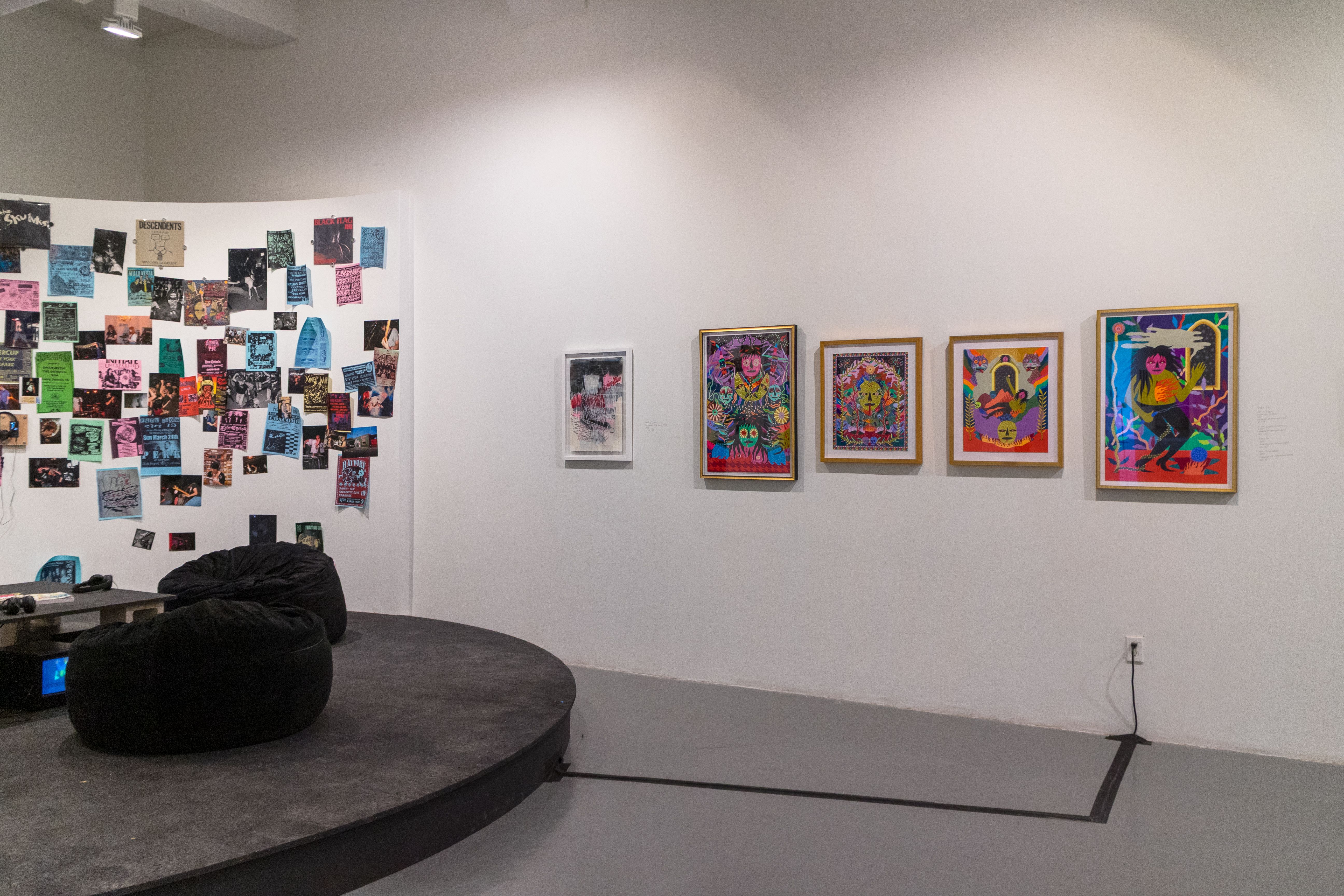 Bright paintings are shown on the wall next to the Mosh Pit, which is a wall covered in community show posters and a stage with beanbags for sitting.