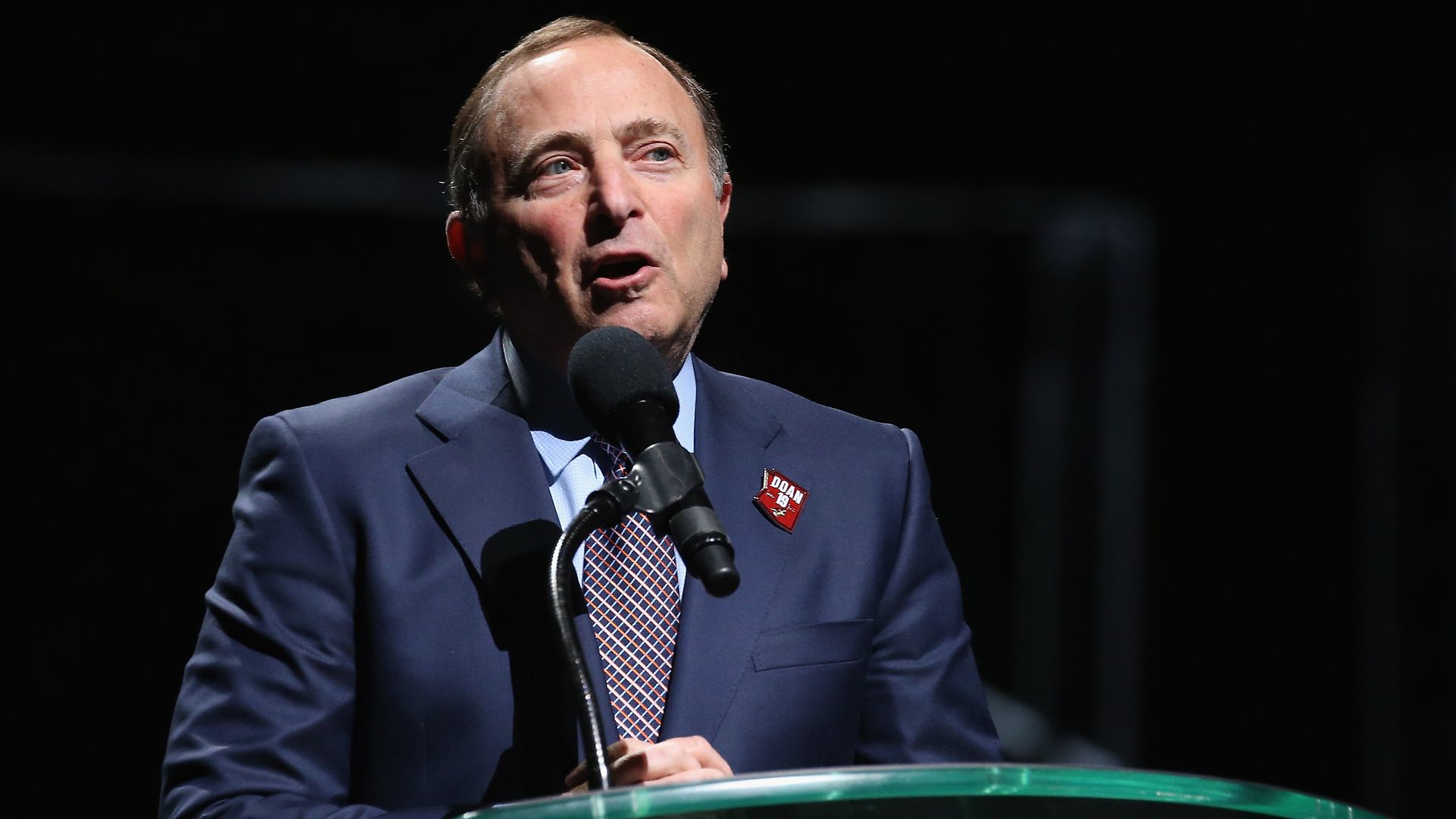 NHL commissioner Gary Bettman stands and speaks in a suit in front of a podium.