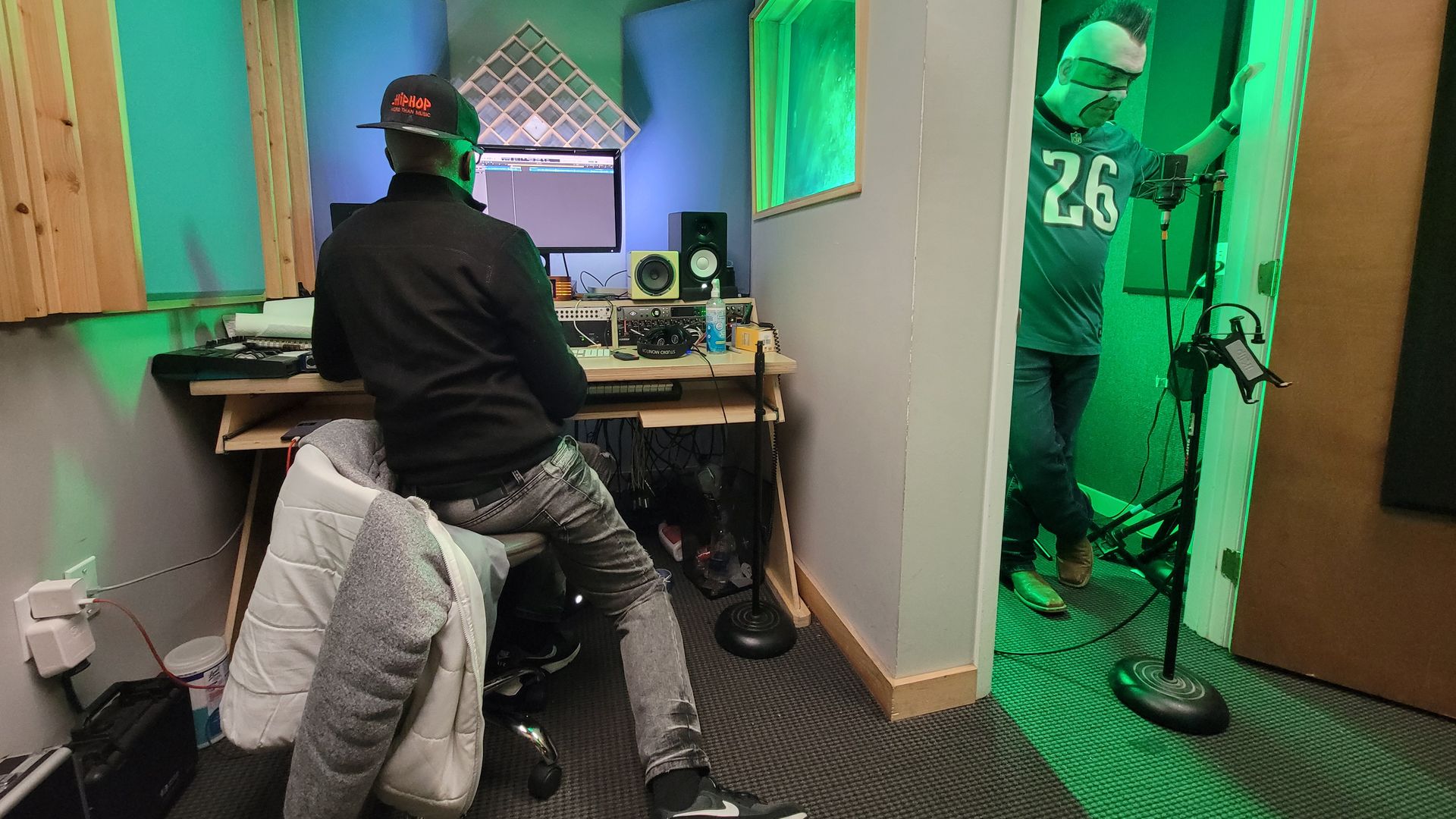 Left to right: Music producer Herb Middleton seated at a computer with audio equipment; Jamie Pagliei, aka the Philly Sports Guy, standing in a vocal booth.