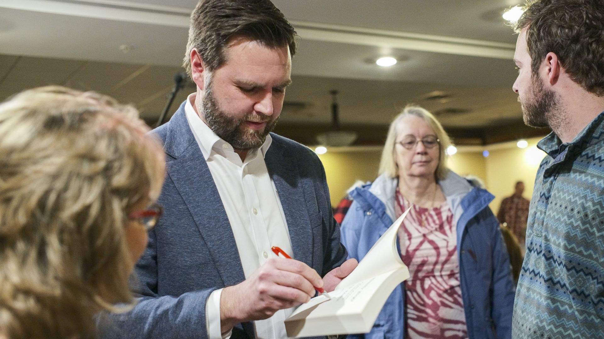 JD Vance signs a copy of a book for a woman who looks on.