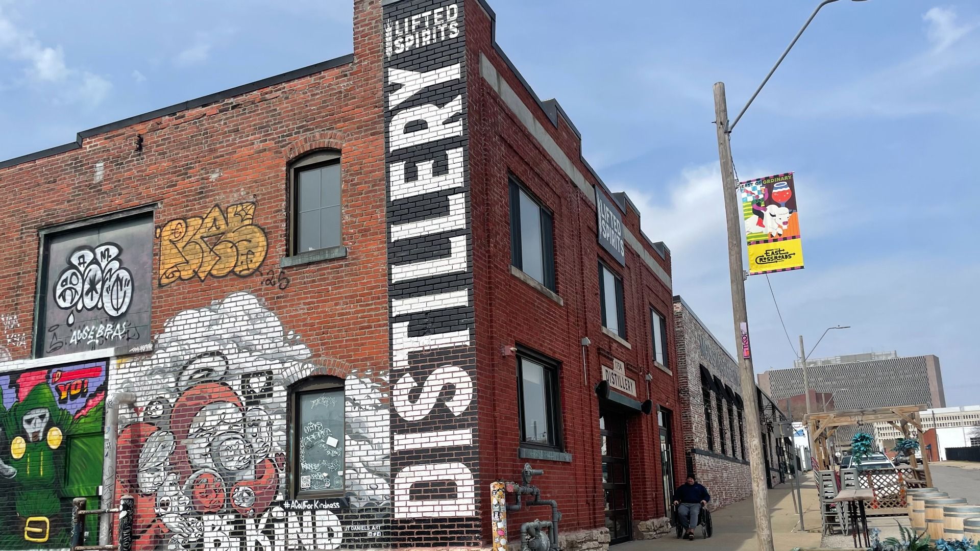 Red brick building with a large vertical DISTILLERY sign on the corner, colorful graffiti murals on the wall, and a clear blue sky above.
