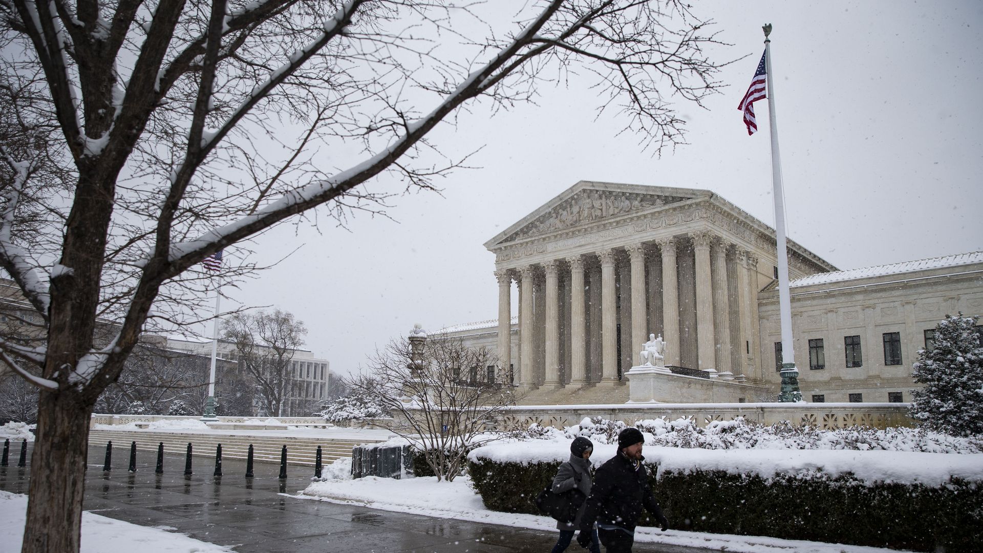 In this image, pedestrians walk on a snowy sidewalk in front of the Supreme Court. 