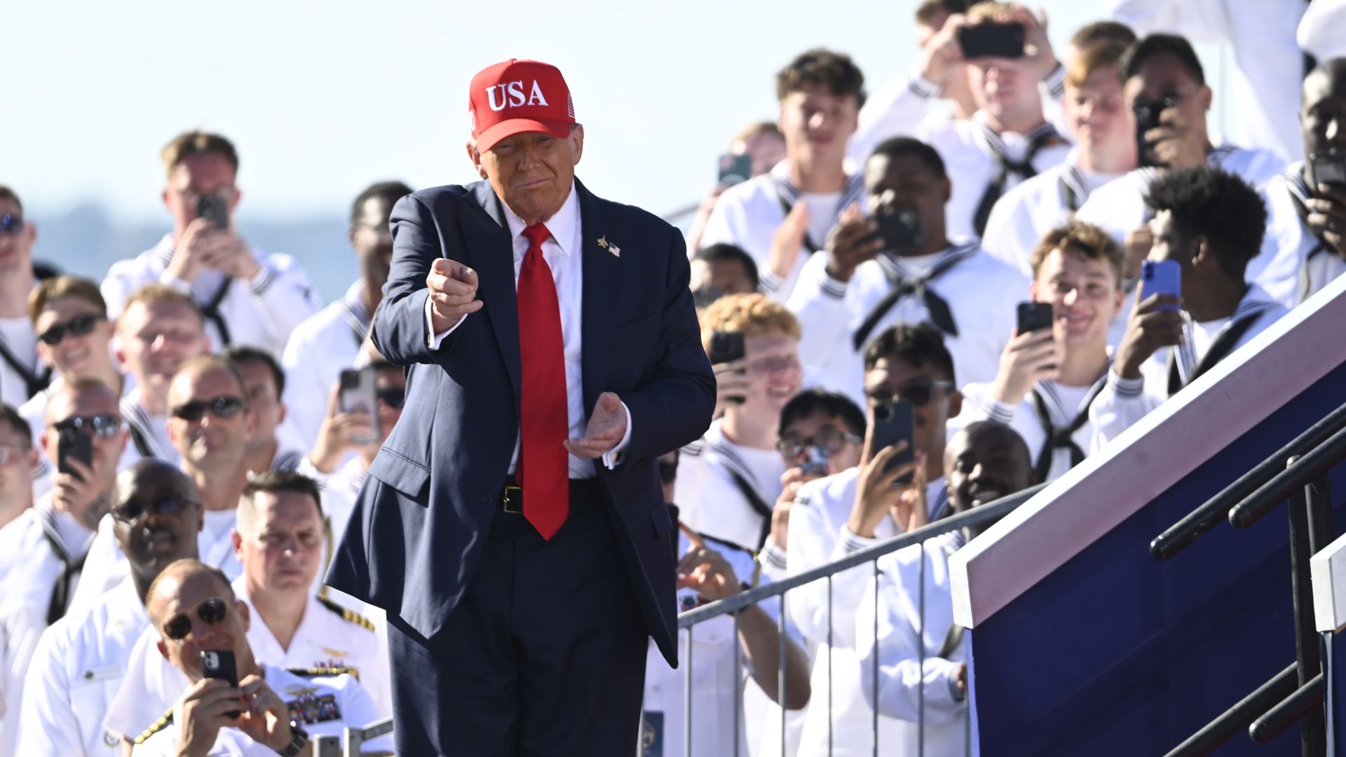 President Trump, standing in front of white-uniformed sailors, many of whom are holding phones and cameras, points at a celebration for the U.S. Navy's 250th anniversary at Naval Station Norfolk in Norfolk, Virginia, on Sunday. Photo: Kyle Mazza/Anadolu via Getty Images