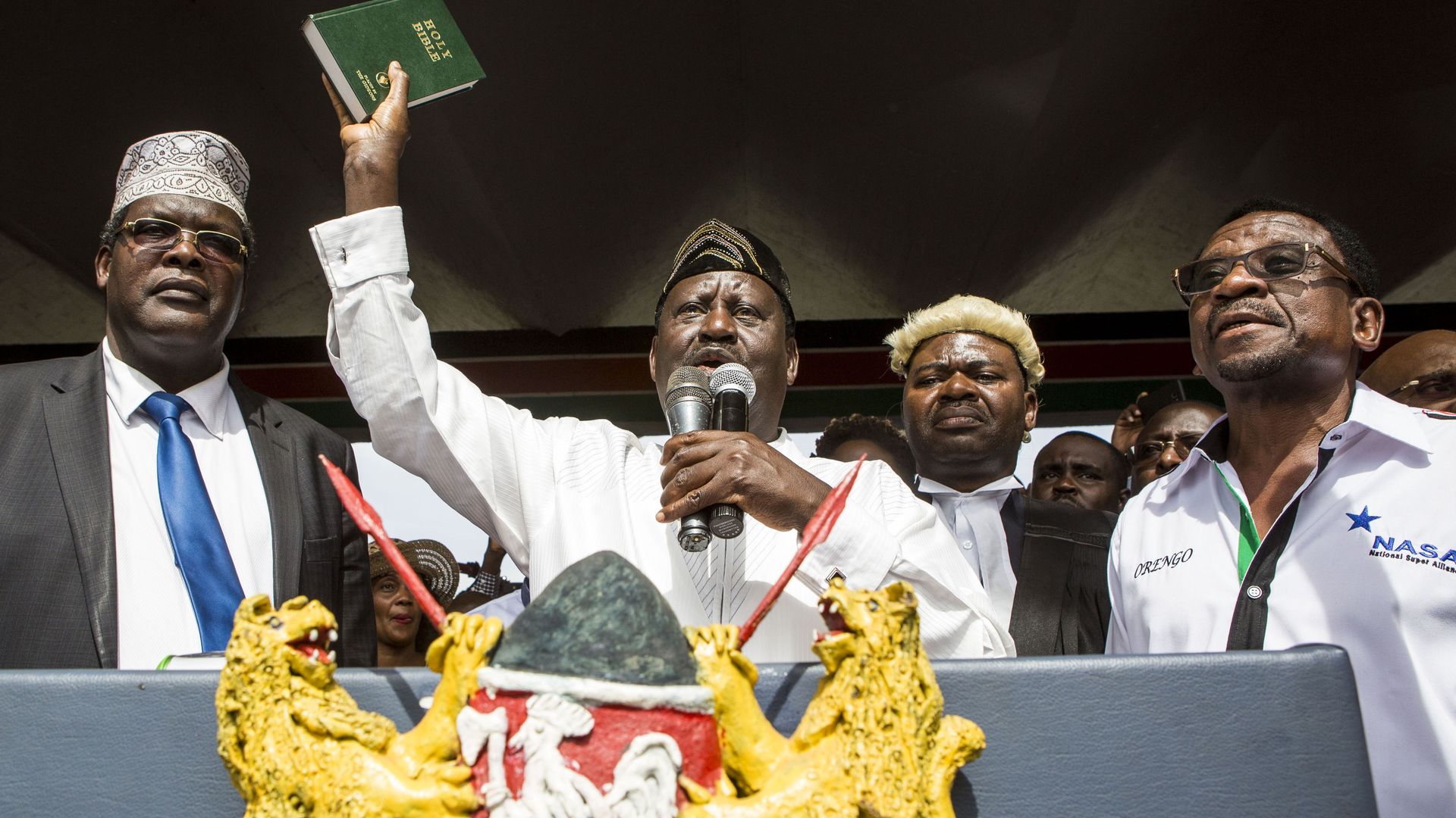 Odinga with Bible raised while speaking at lectern