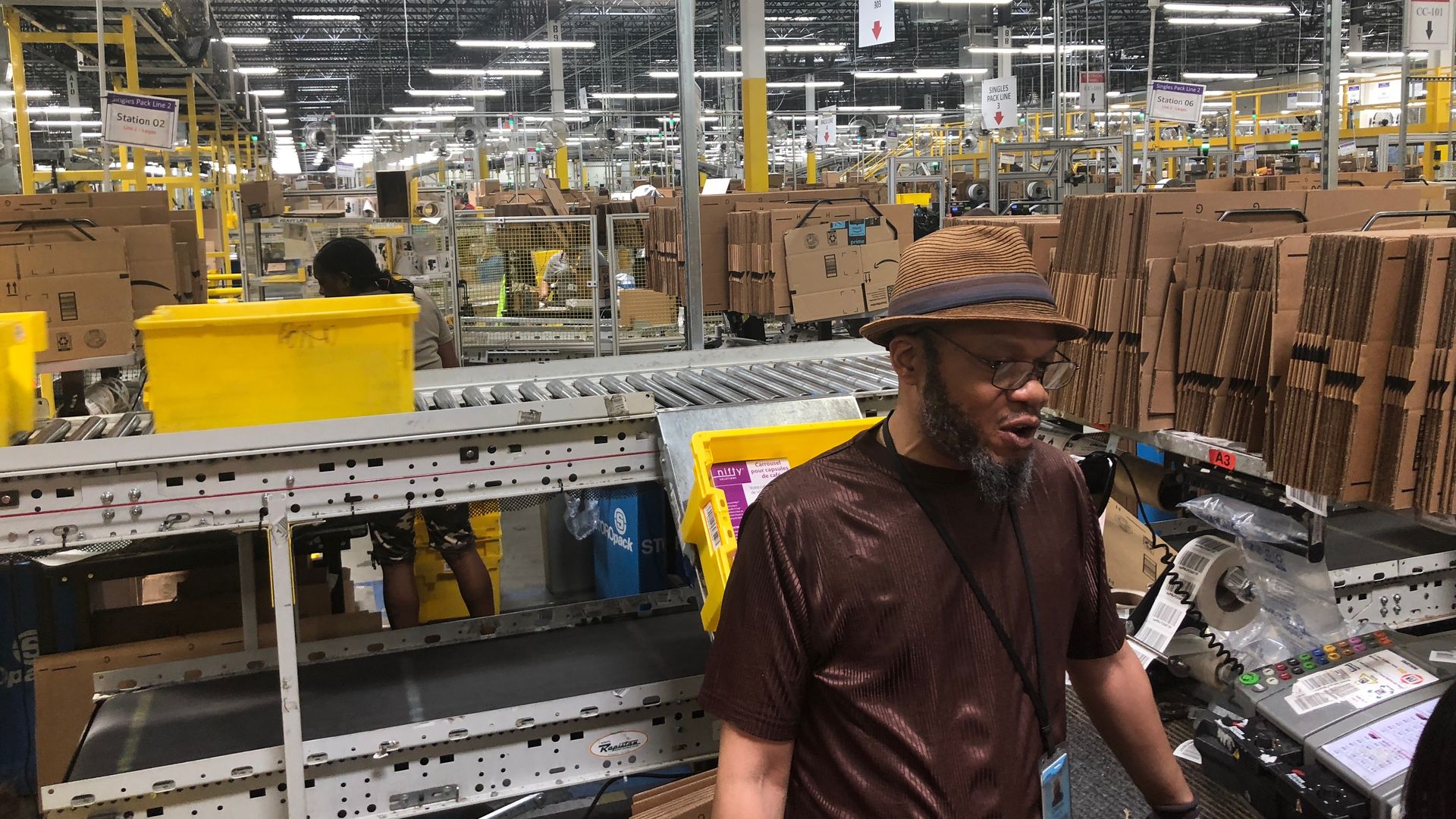 A man stands next to a conveyer belt with Amazon packages on it