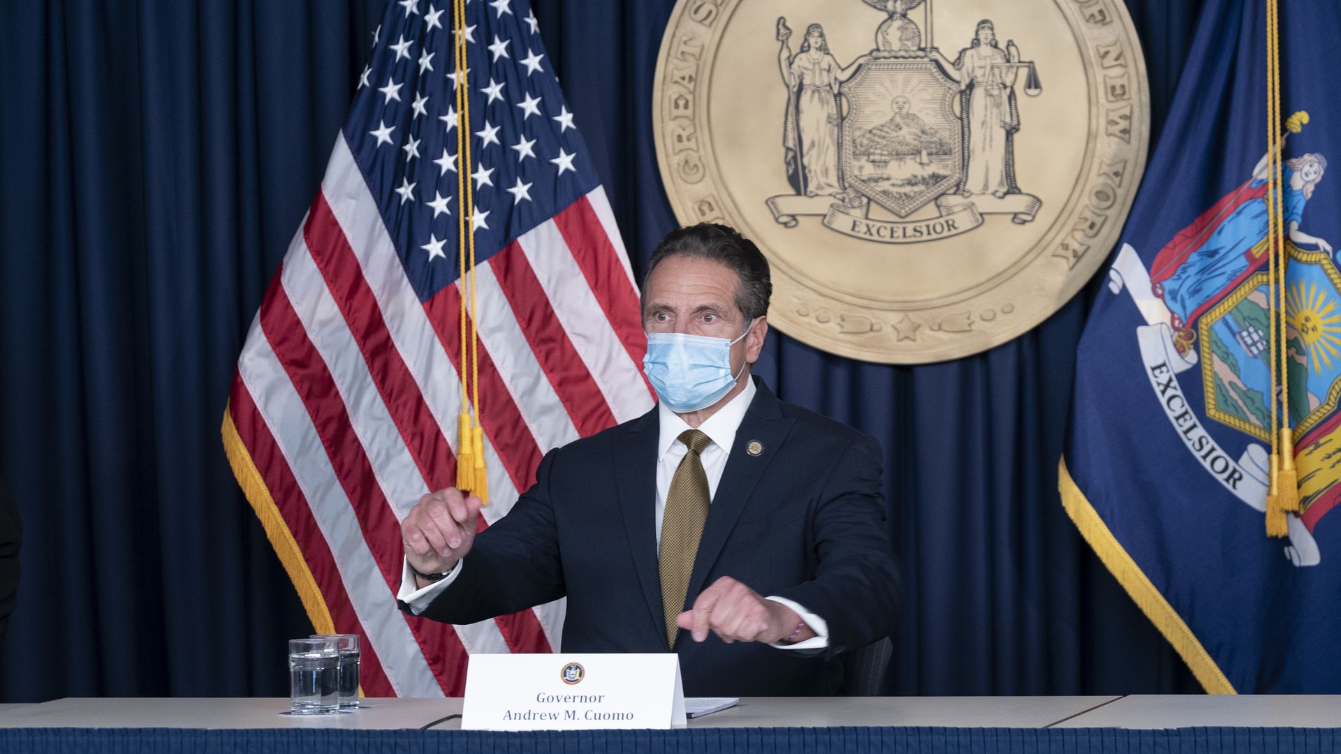 Cuomo wears a face mask in front of an American flag and New York state crest