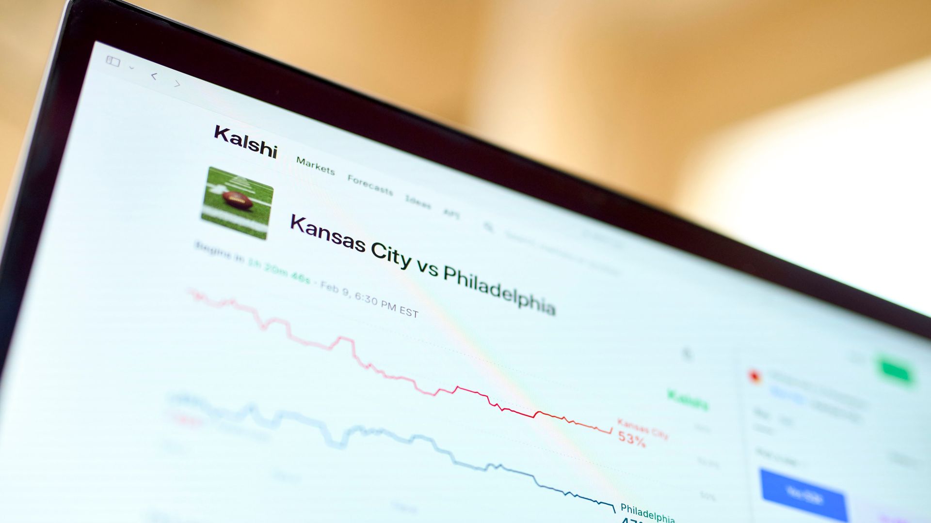 Close-up of a laptop screen showing a Kalshi market page with the headline "Kansas City vs Philadelphia" and a red downward stock chart along with a small football image.